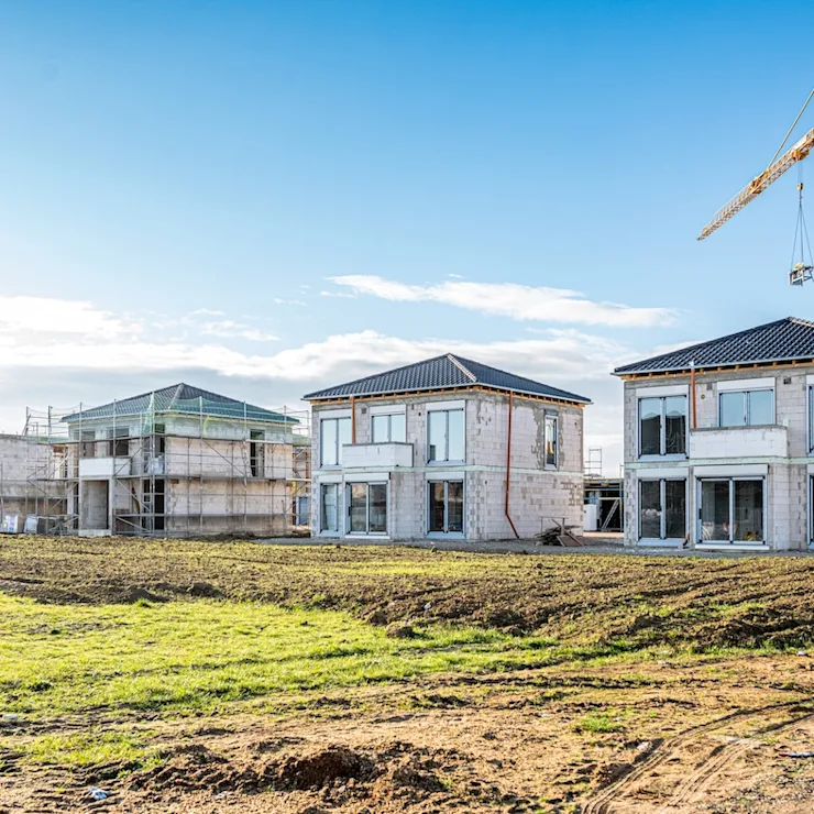 Mehrere Einfamilienhäuser im Rohbau mit Baukran und Gerüsten auf einer Baustelle.