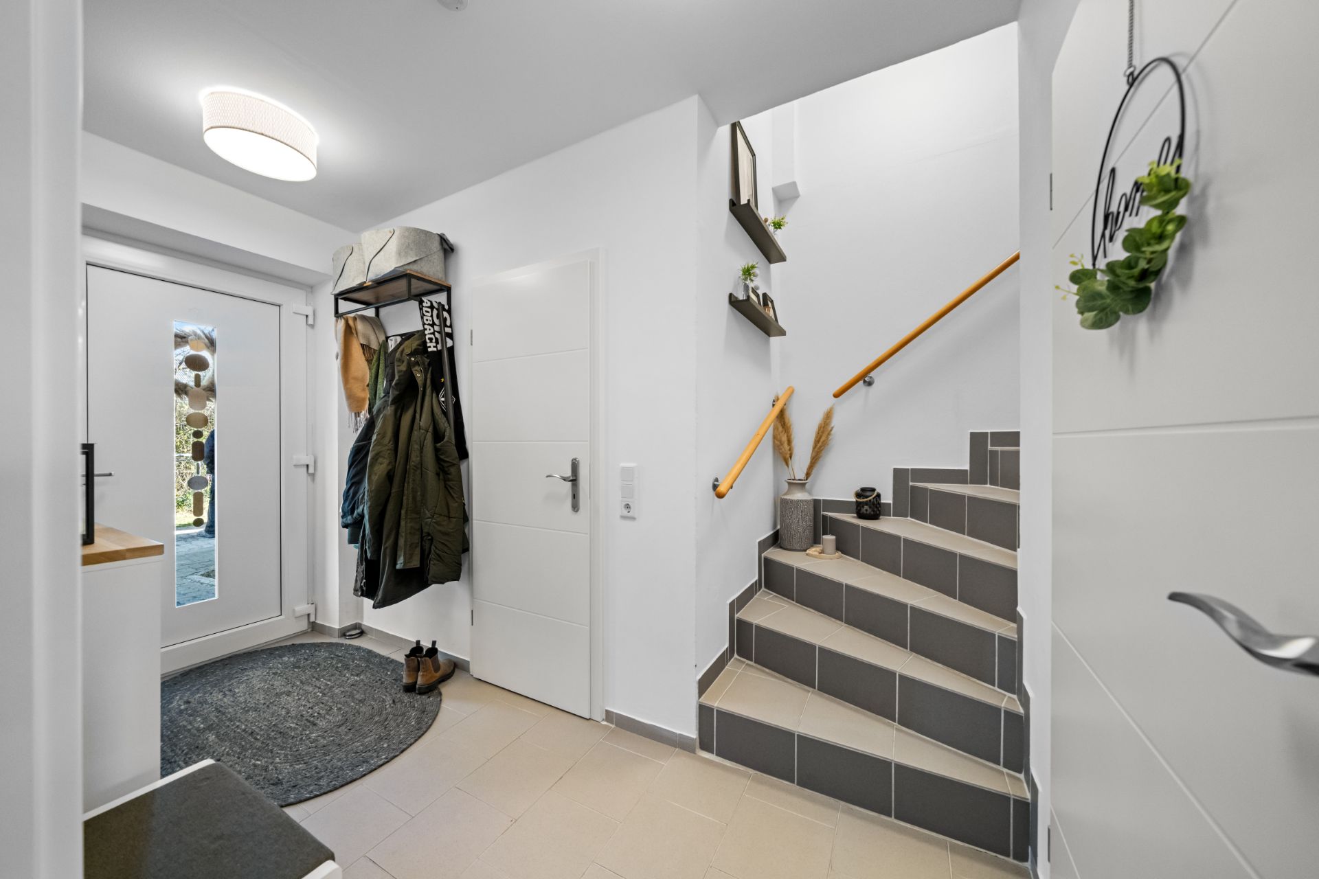 Heller Flur mit Garderobe, Treppe und Haustür, Jacken und Schuhe sind sichtbar.
