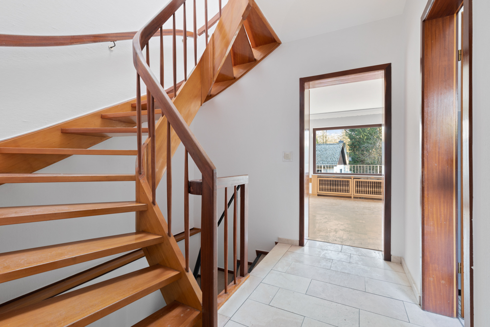 Heller Flur mit Holztreppe und Blick auf einen Balkon mit Ausblick auf Bäume.