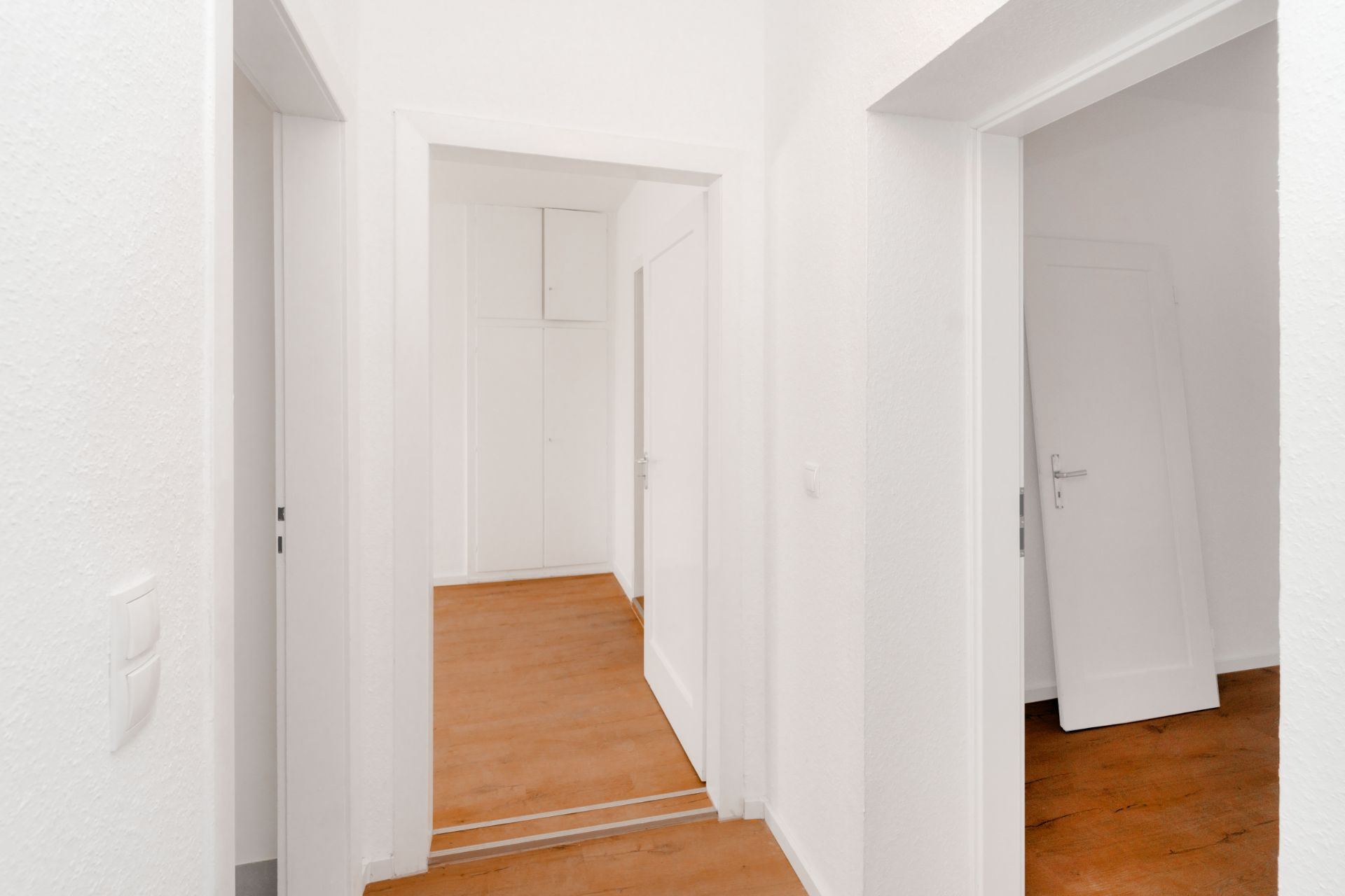 Heller Flur mit Holzboden und mehreren offenen Türen in einer Wohnung.