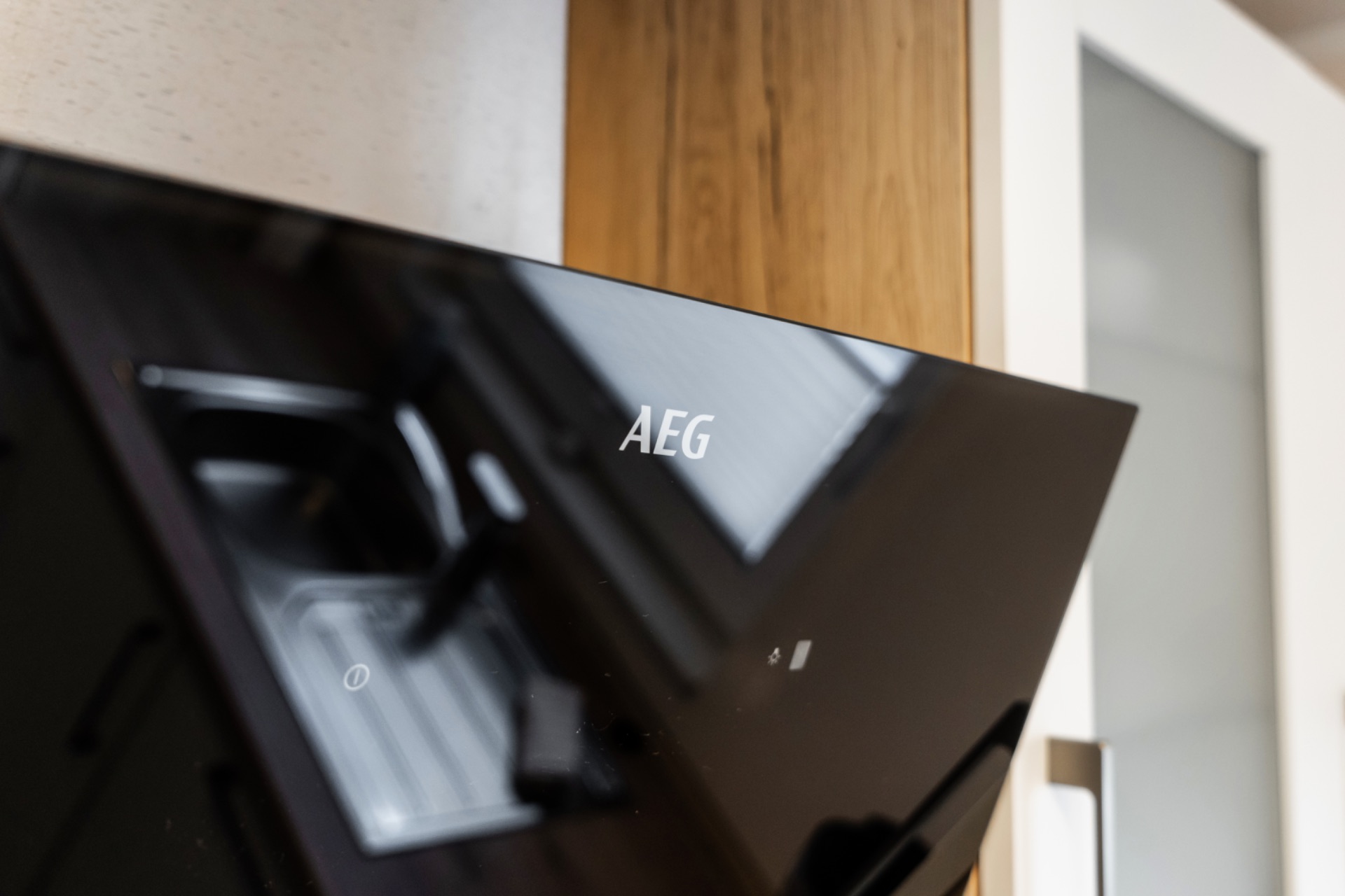 Schwarze Dunstabzugshaube mit AEG-Logo vor Holzschrank und Glastür.