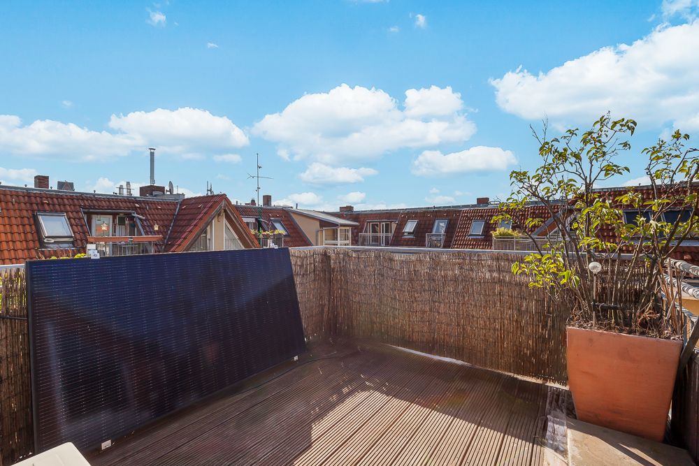 Kleine Dachterrasse mit Solarpanel, Pflanze im Topf und Blick auf Häuser mit roten Dächern.