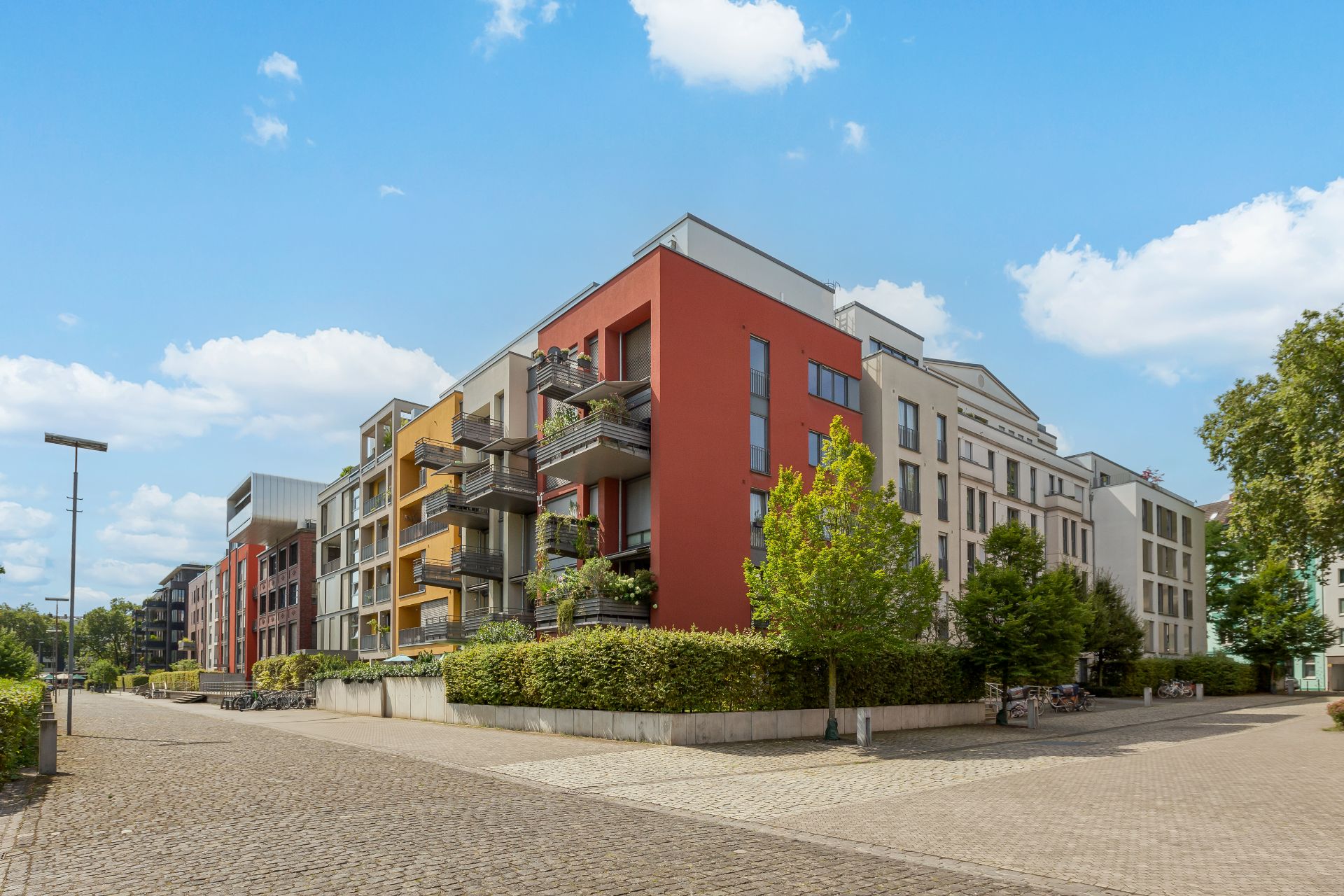 Moderne Mehrfamilienhäuser mit Balkonen und bunten Fassaden an einer ruhigen Straße.