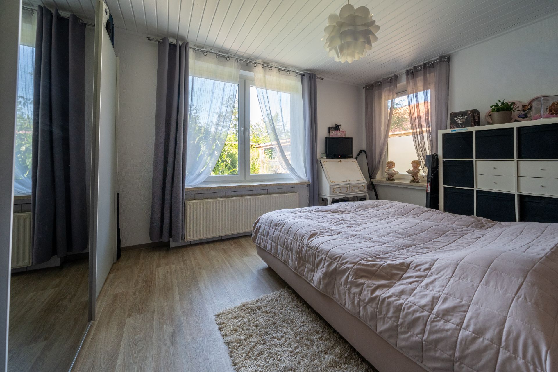 Helles Schlafzimmer mit Doppelbett, großem Fenster, Schreibtisch und Kommode.