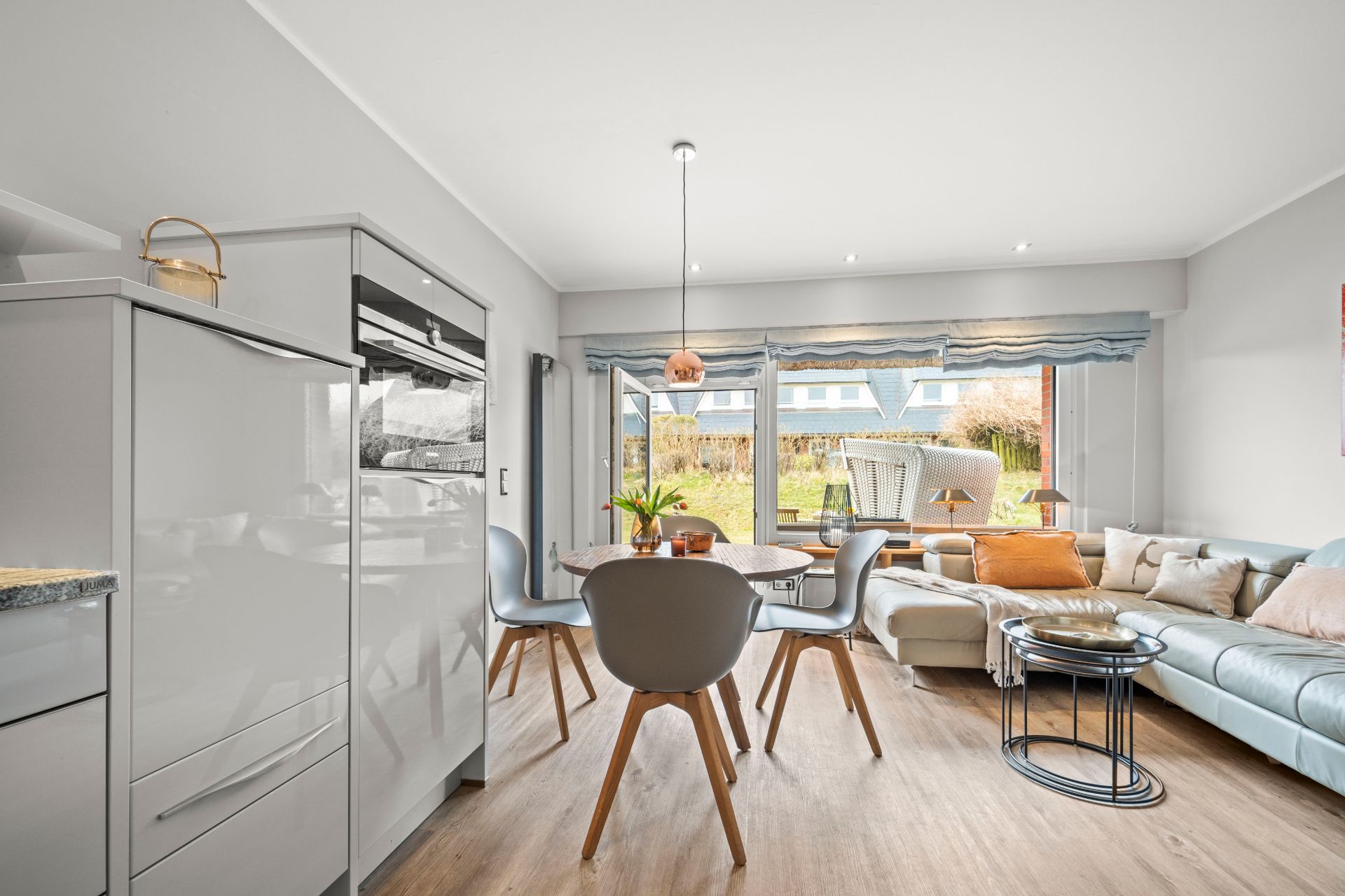 Helles Wohnzimmer mit Essbereich und moderner Küche, große Fenster mit Blick auf den Garten.