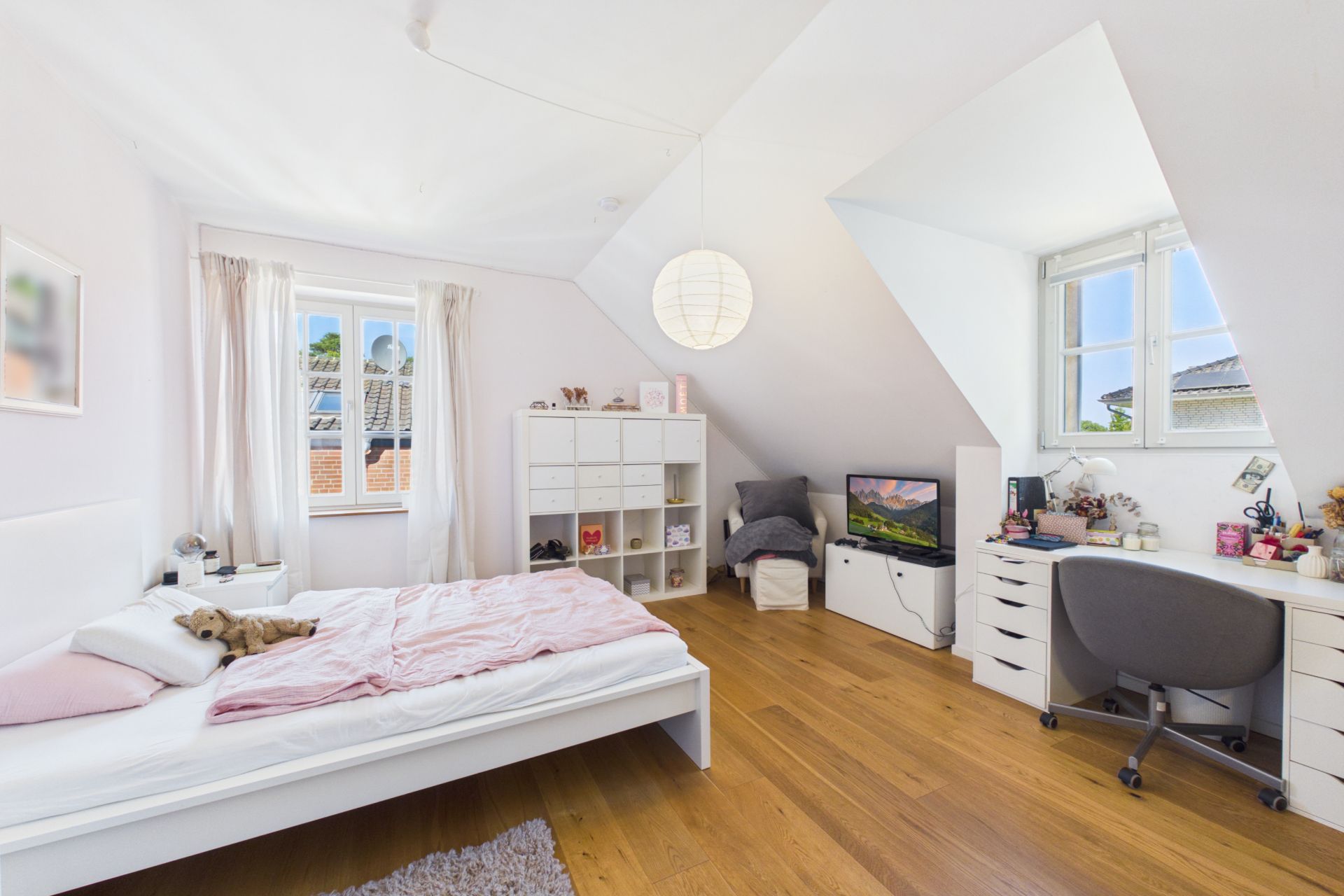 Helles Schlafzimmer mit Bett, Regal, Schreibtisch und Holzfußboden unter Dachschrägen.