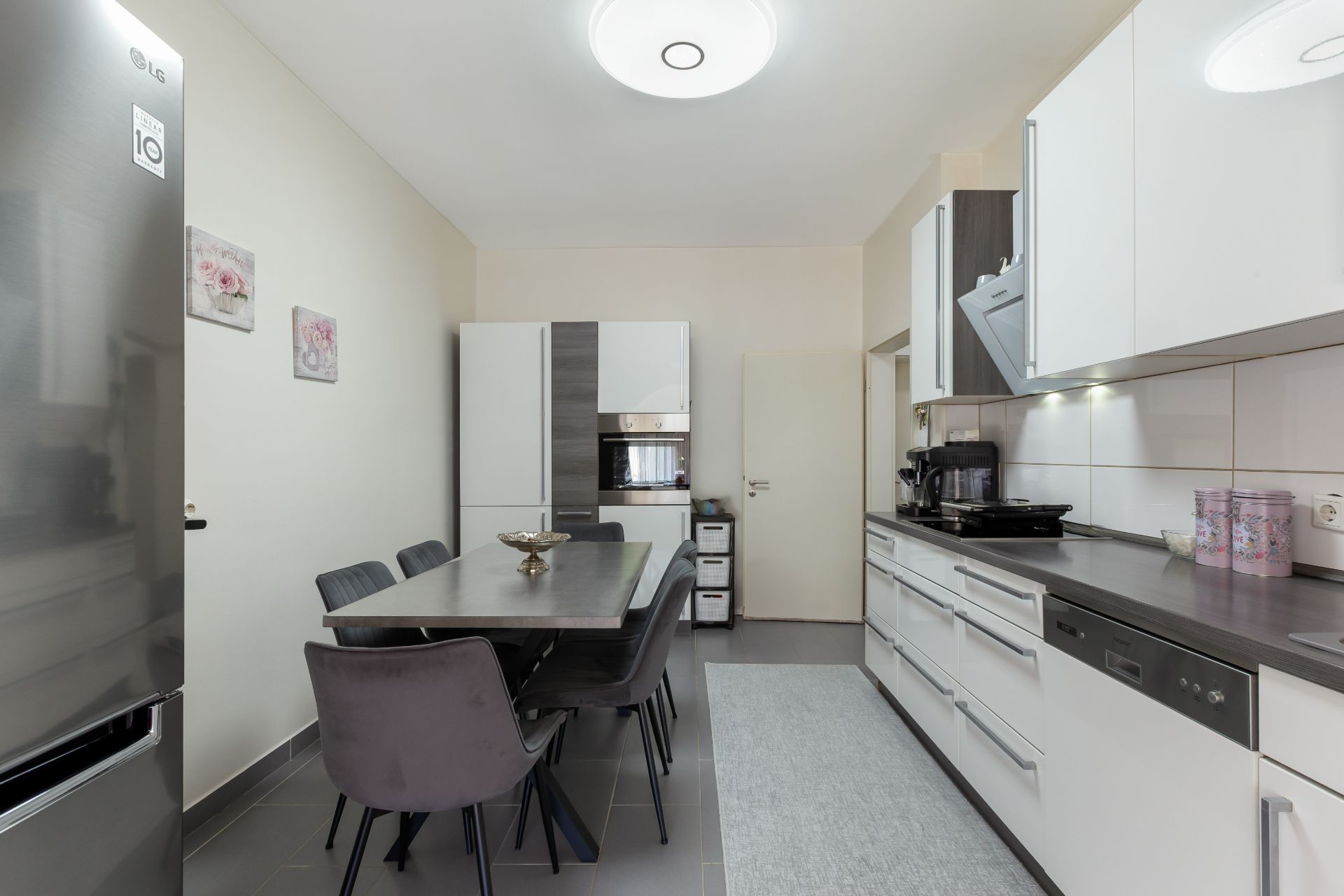 Moderne Küche mit Esstisch, sechs Stühlen, Kühlschrank und weißen Schränken.