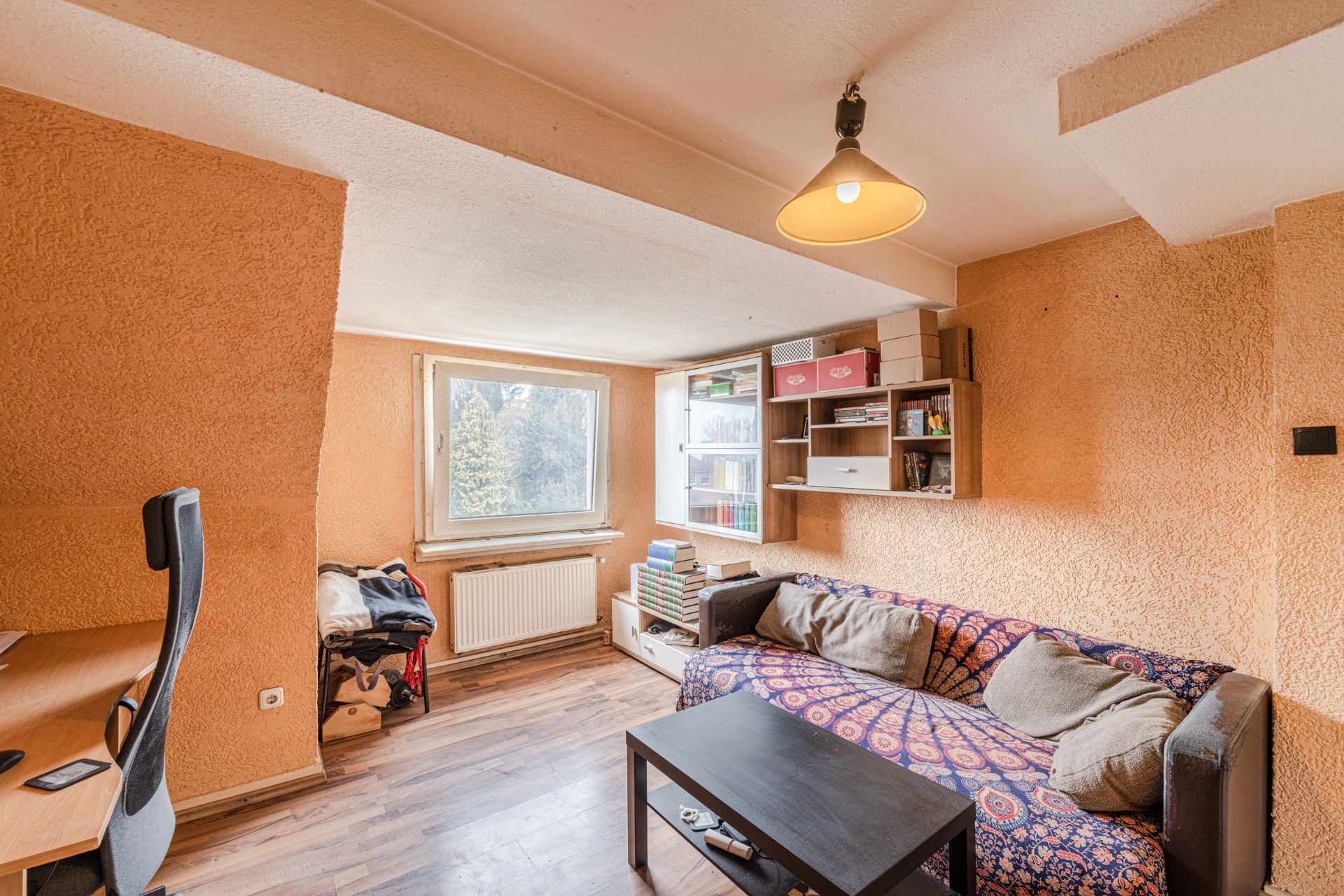 Wohnzimmer mit Sofa, Couchtisch, Schreibtisch und Regal an orange gestrichenen Wänden.