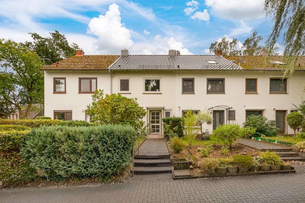 Mehrfamilienhaus mit Vorgarten, Treppe zum Eingang und gepflegten Büschen.