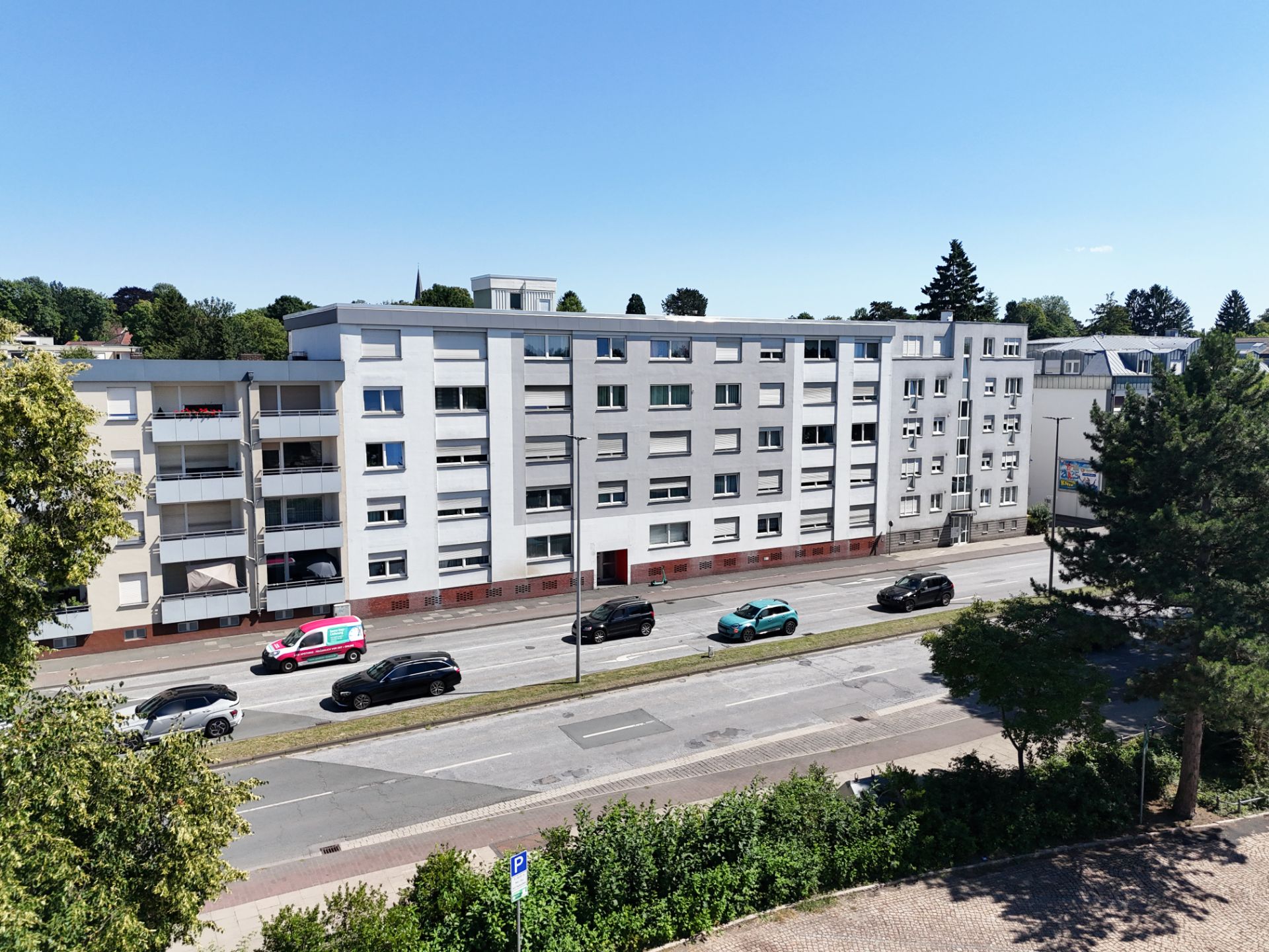 Mehrstöckiges Wohnhaus mit Balkonen an einer Straße, mehrere Autos parken davor.