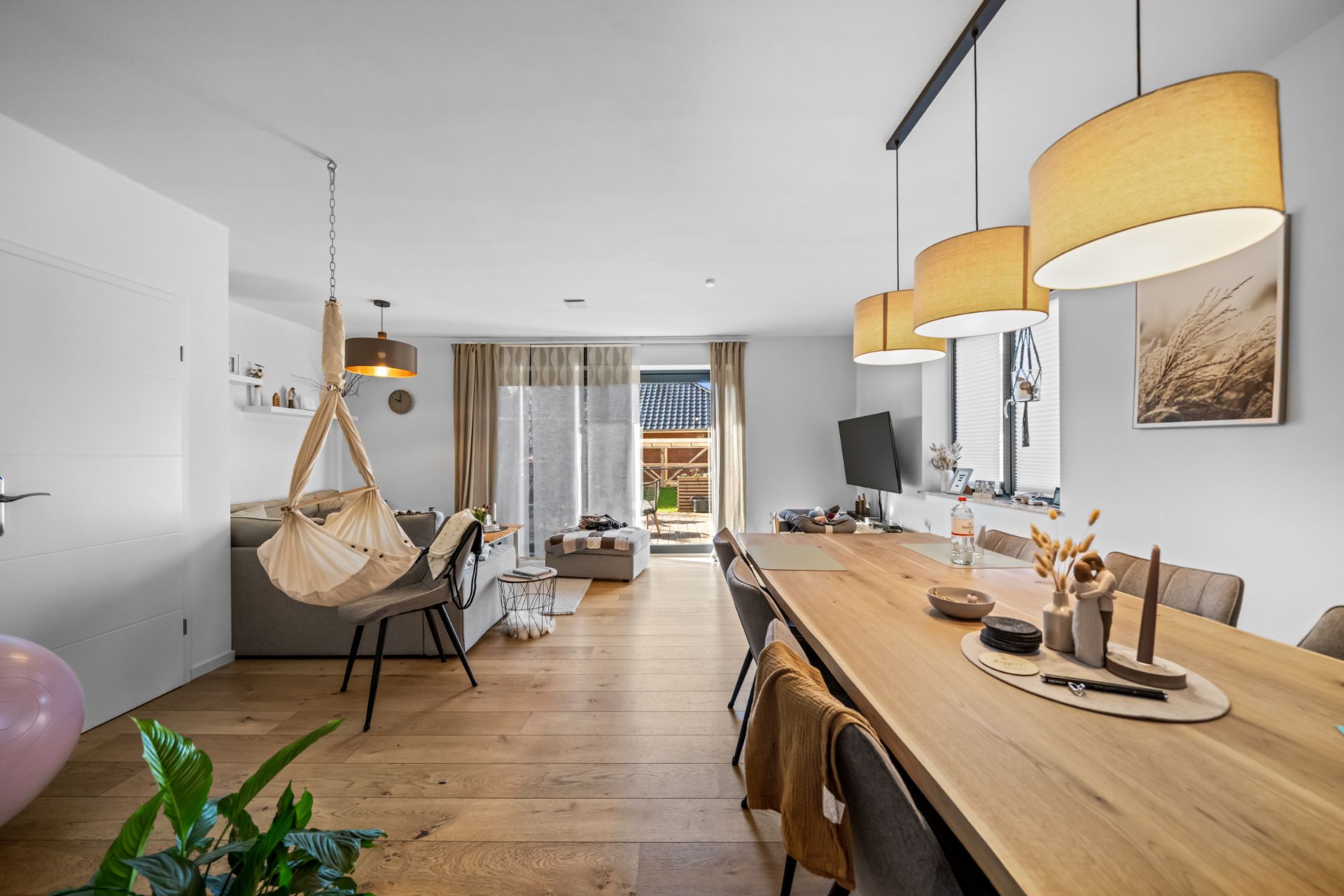 Helles Wohnzimmer mit Hängesessel, Esstisch, Sofa und großen Fenstern zum Garten.