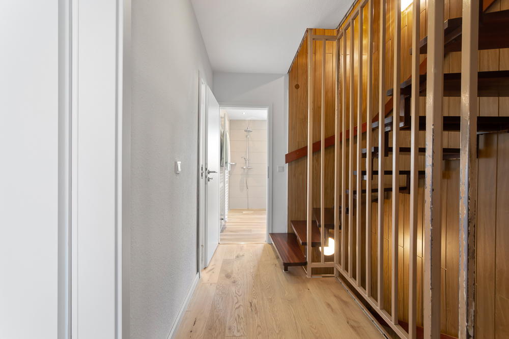 Flur mit Holztreppe und Blick ins Badezimmer mit Dusche.