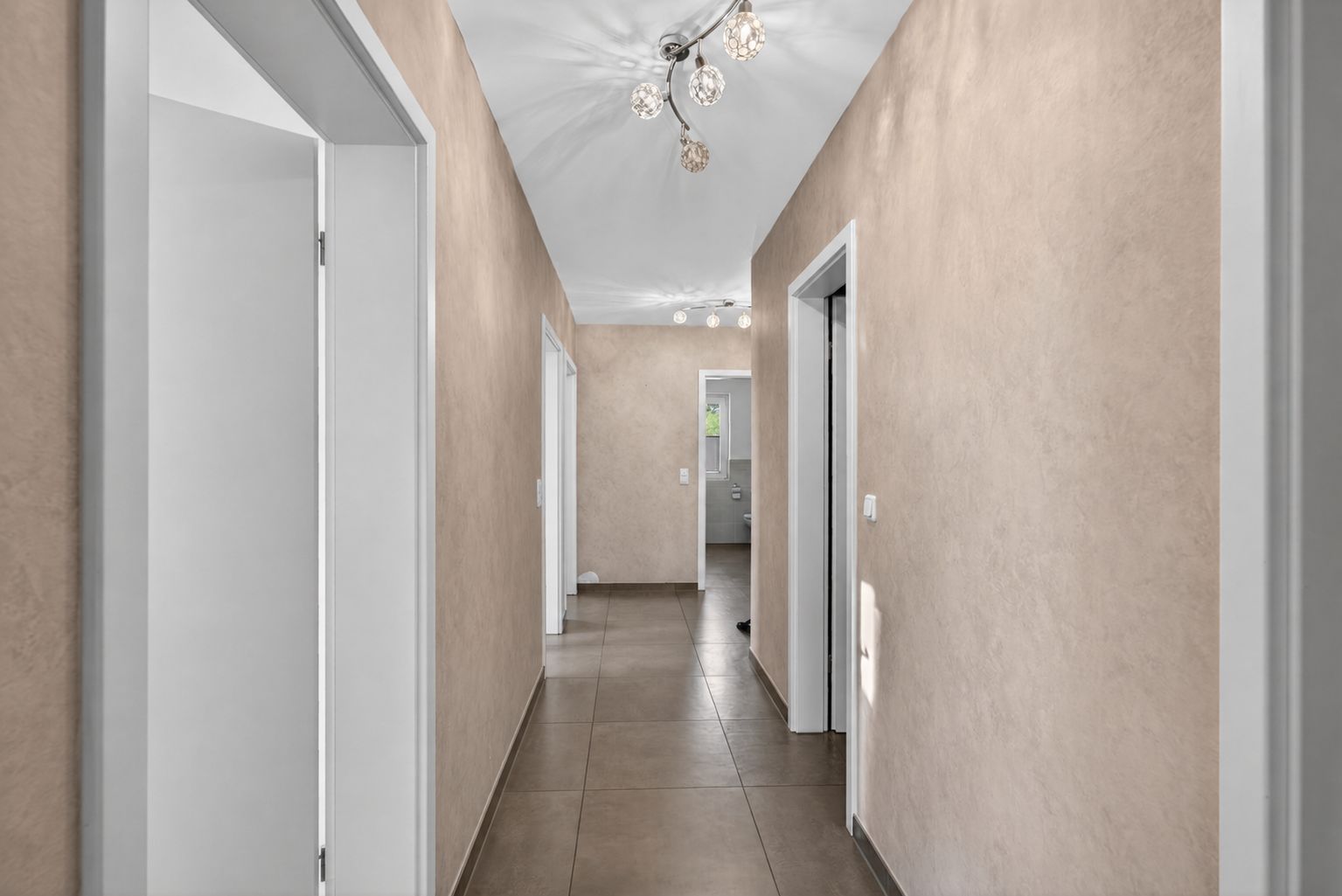 Heller Flur mit beigen Wänden, Fliesenboden und modernen Deckenleuchten.