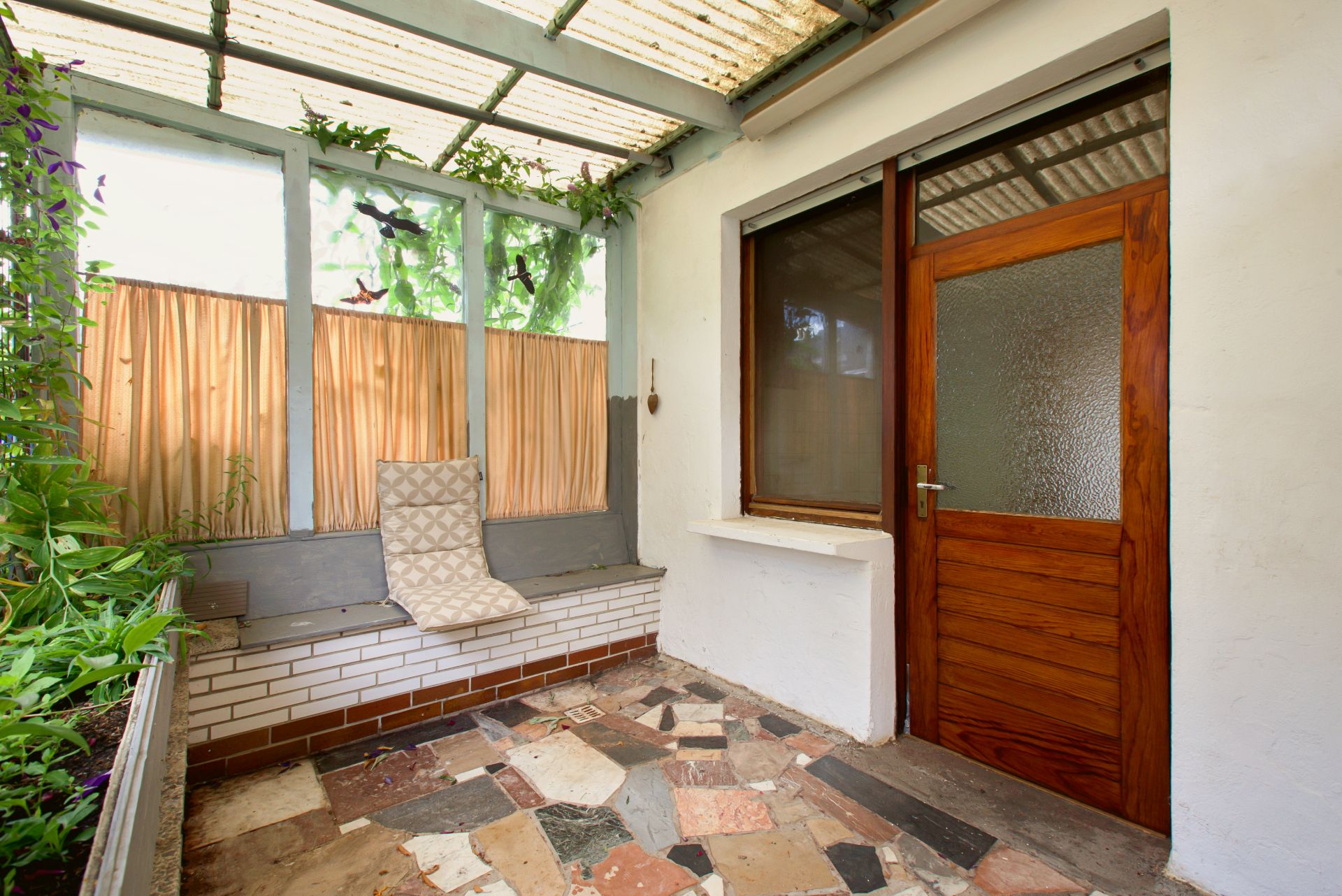 Überdachte Terrasse mit gemischtem Steinboden, Holzbank, Holzfenster und Tür.