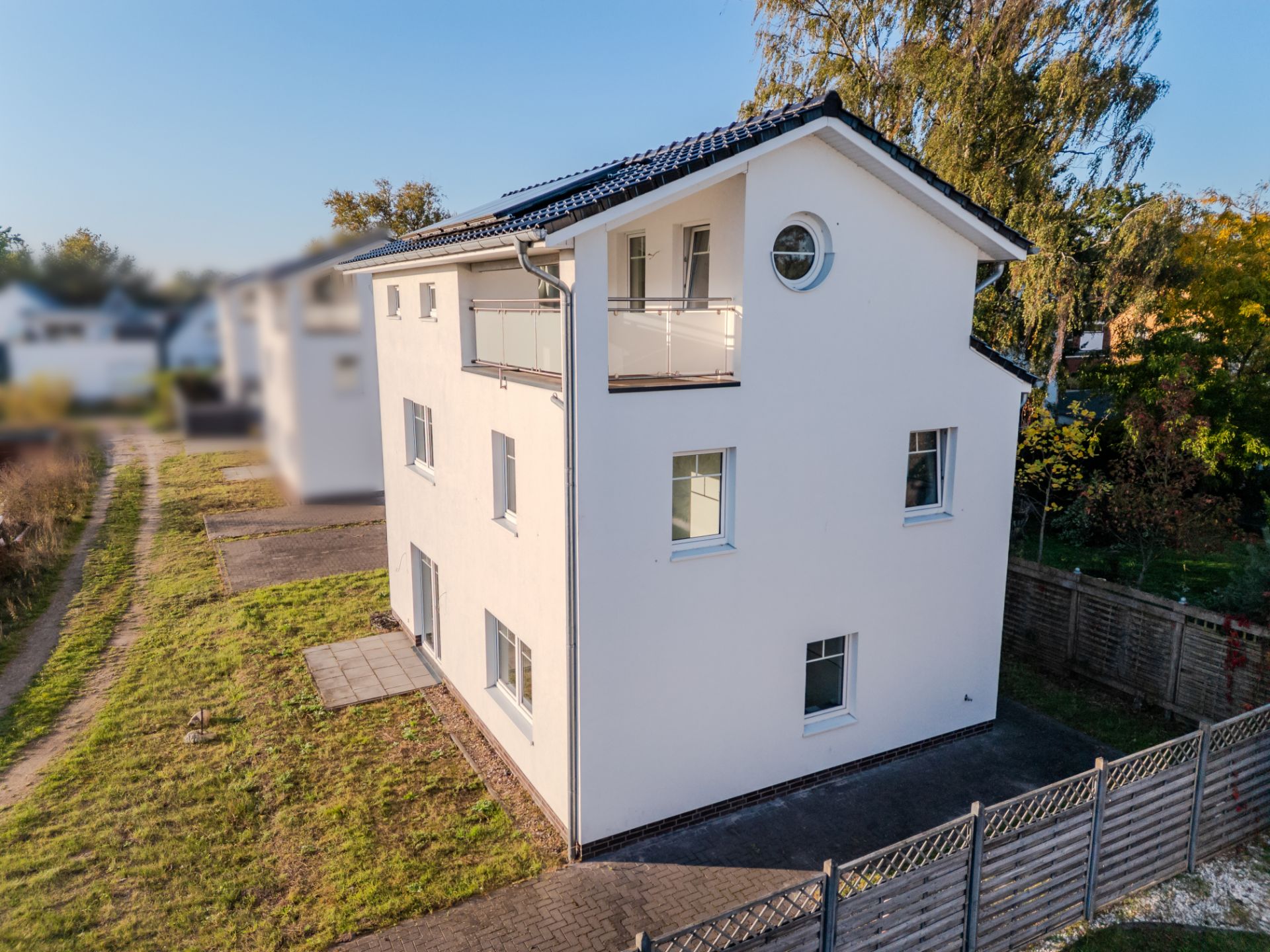 Modernes, dreistöckiges weißes Wohnhaus mit Balkon und umzäuntem Garten.