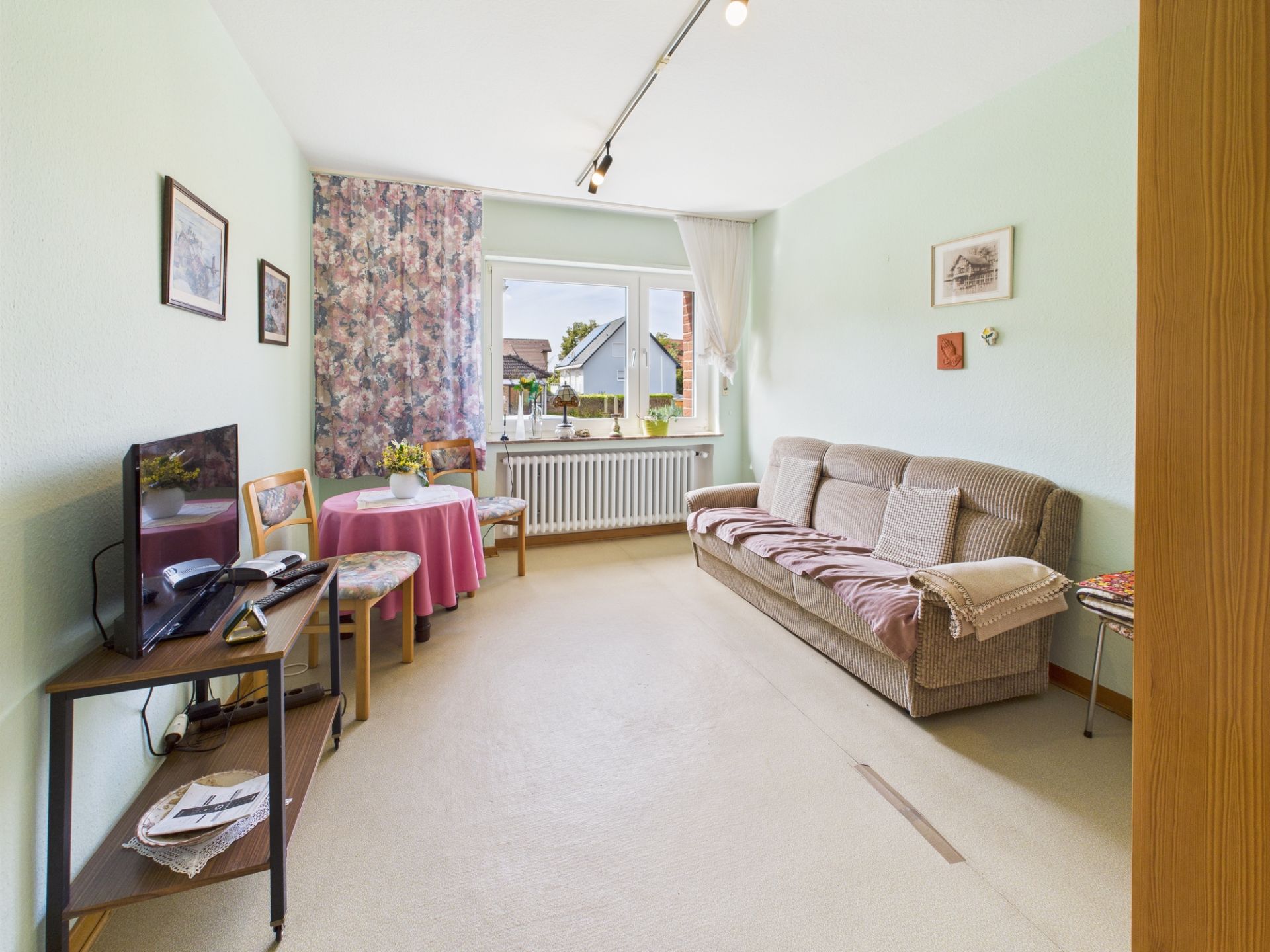 Wohnzimmer mit Sofa, kleinem Tisch, Fernseher und Fenster mit Blick nach draußen.