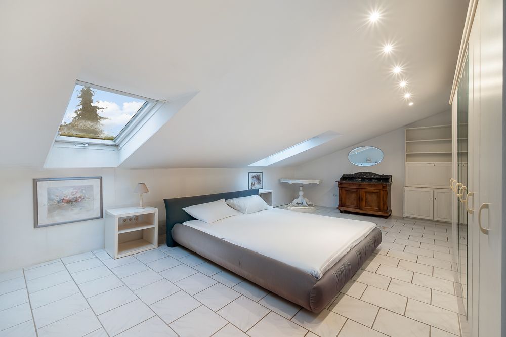 Helles Schlafzimmer mit Dachschräge, Doppelbett, Dachfenstern, Schrank und Kommode mit Spiegel.