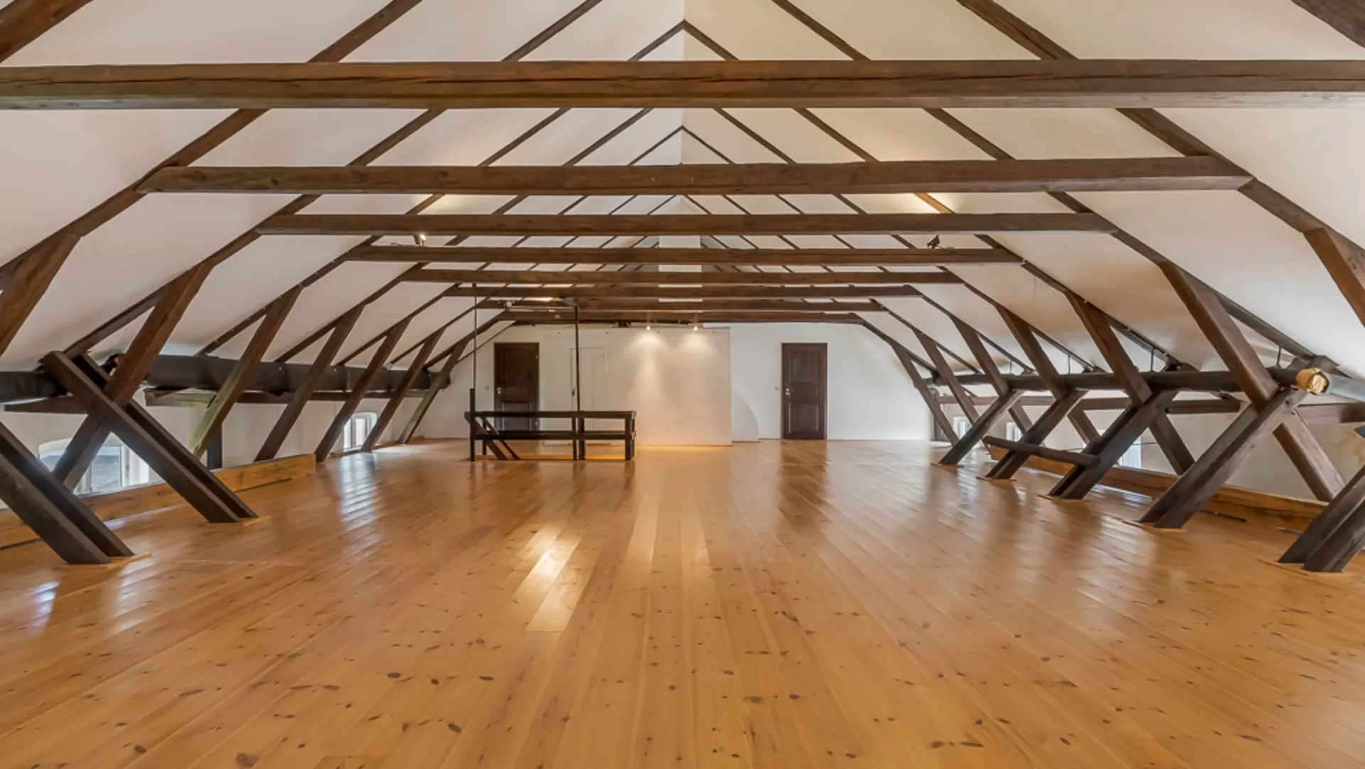 Großer Dachbodenraum mit Holzboden und sichtbaren Holzbalken, weiße Wände, Fenster und Tür im Hintergrund.