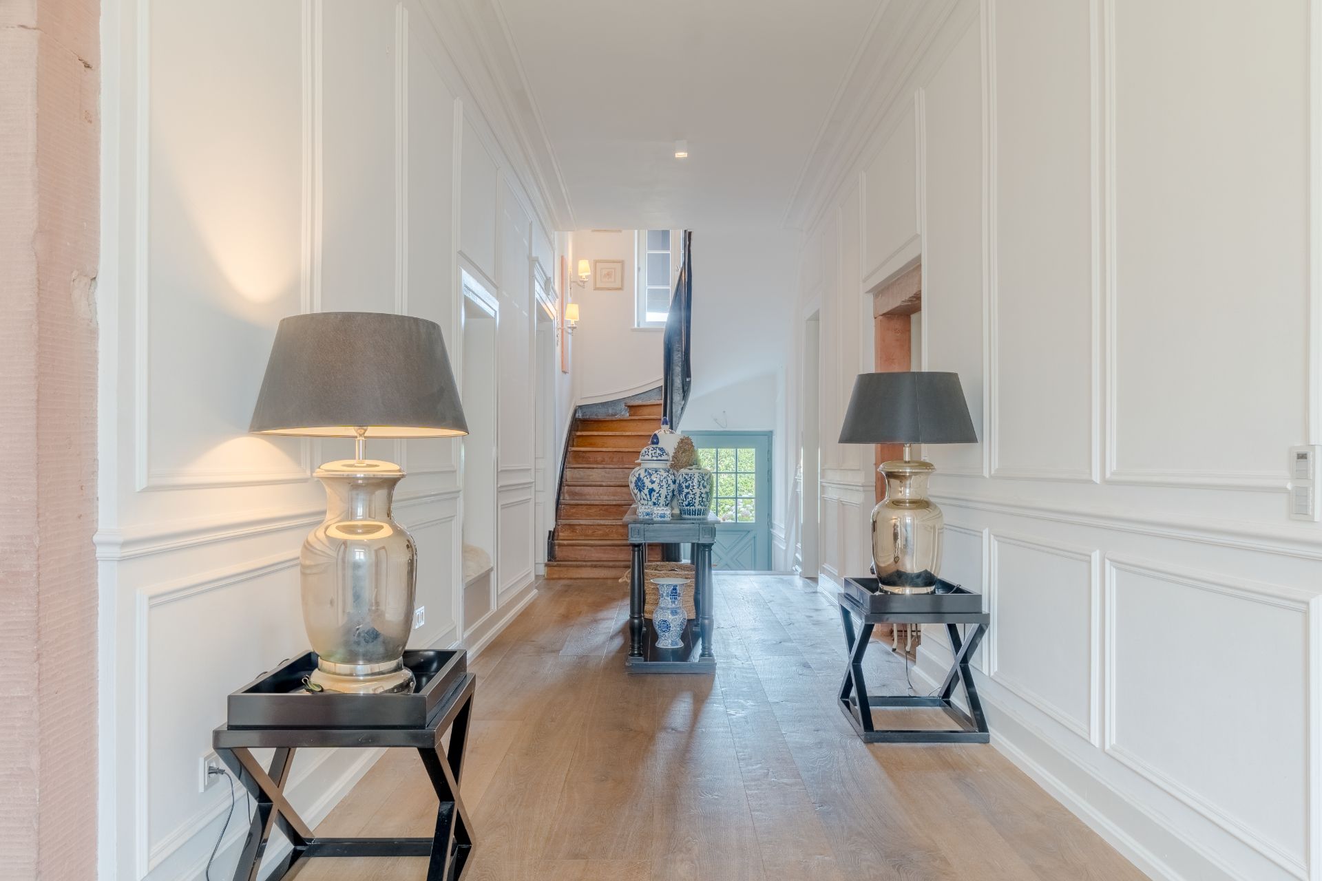 Heller Flur mit zwei Tischlampen, Holzfußboden und Treppe im Hintergrund.