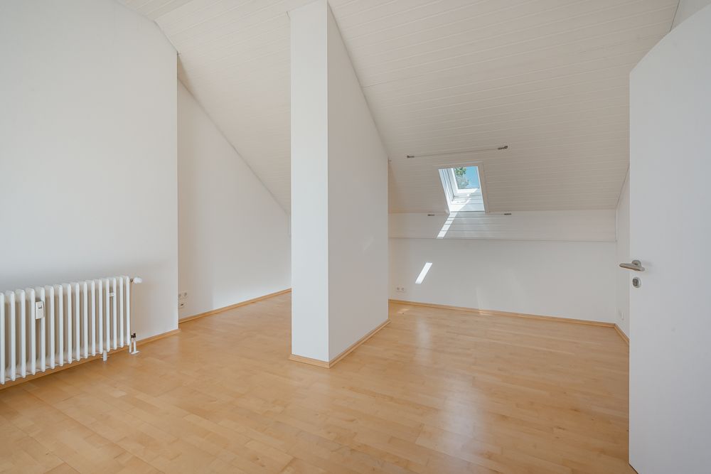 Heller Dachraum mit Holzfußboden, Heizkörper und Dachfenster, durch eine Wand geteilt.