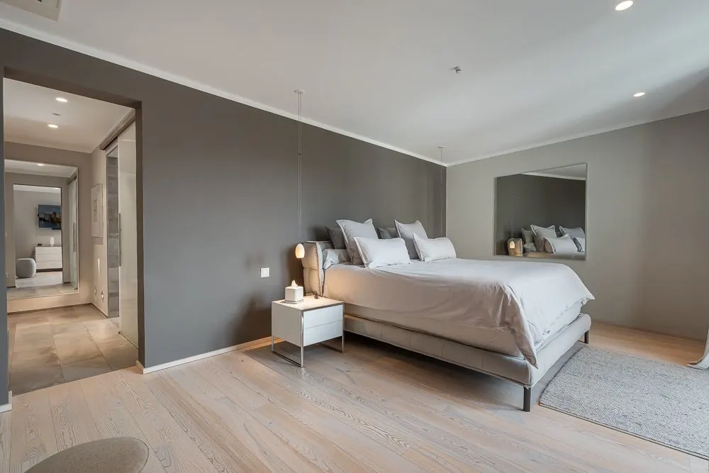 Modernes Schlafzimmer mit großem Bett, Nachttisch und Spiegel an der Wand.