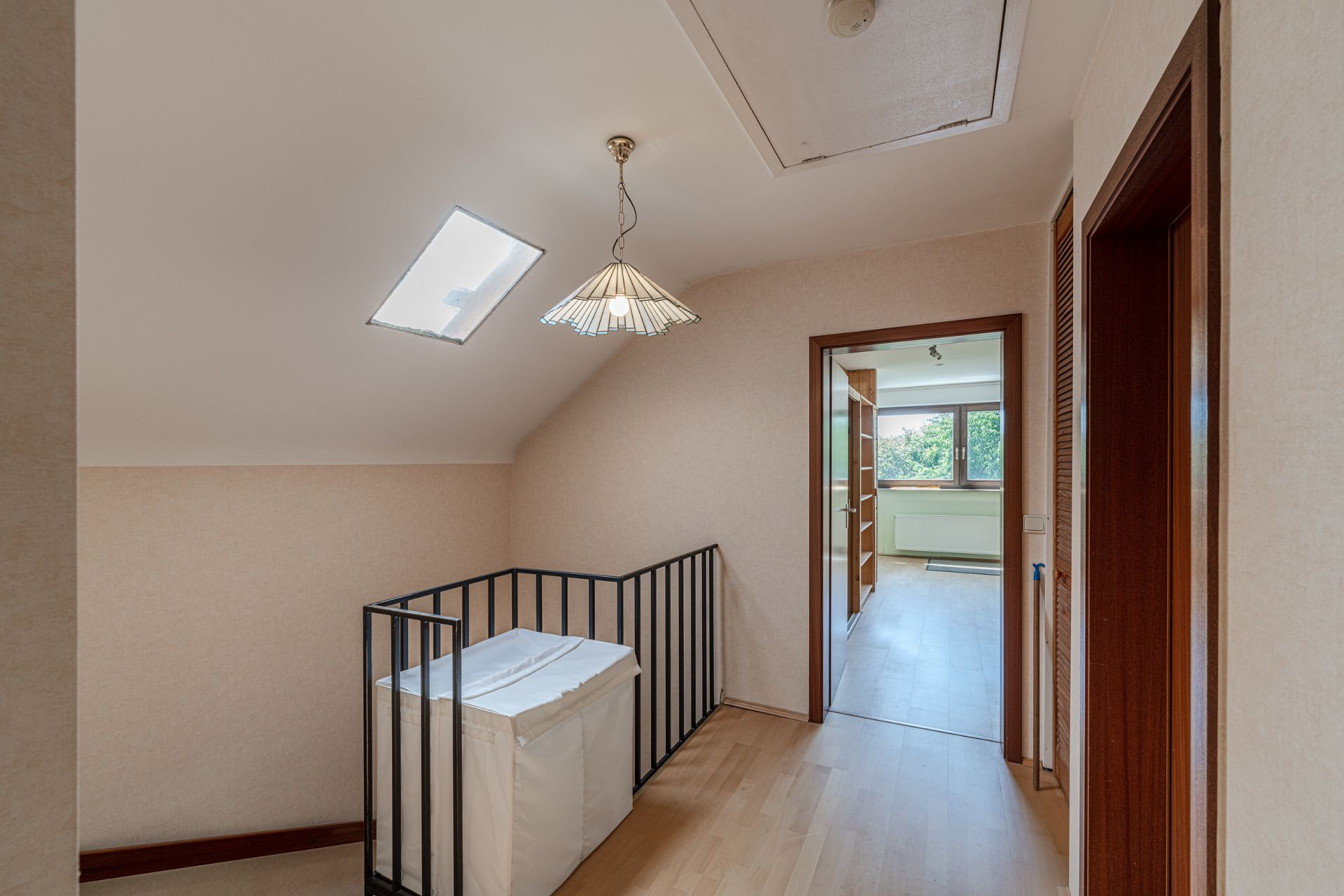 Flur mit Dachfenster, Hängelampe, Treppengeländer und Blick in ein helles Zimmer.