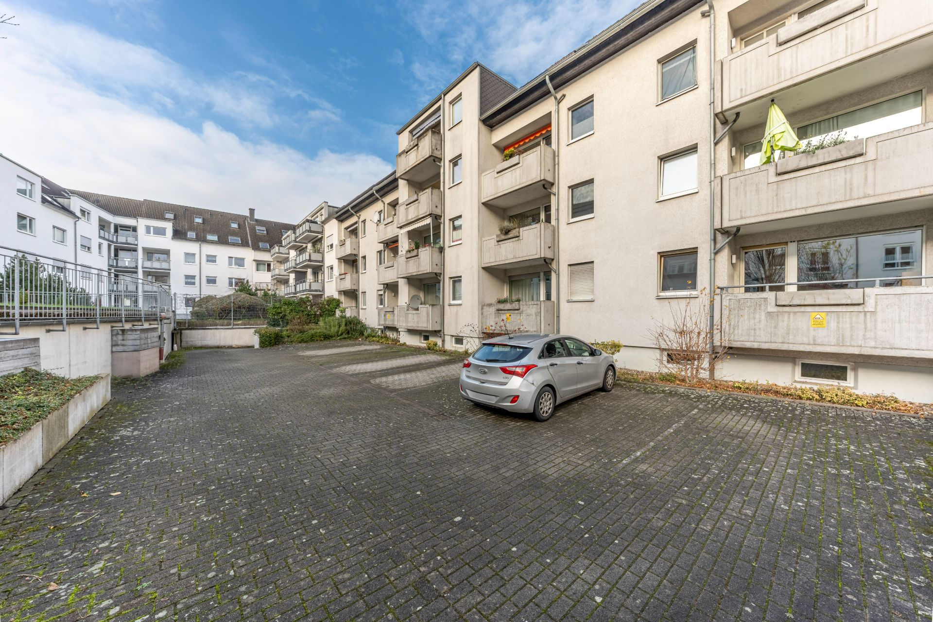 Wohnhaus mit mehreren Balkonen und einem Parkplatz mit einem geparkten Auto im Vordergrund.