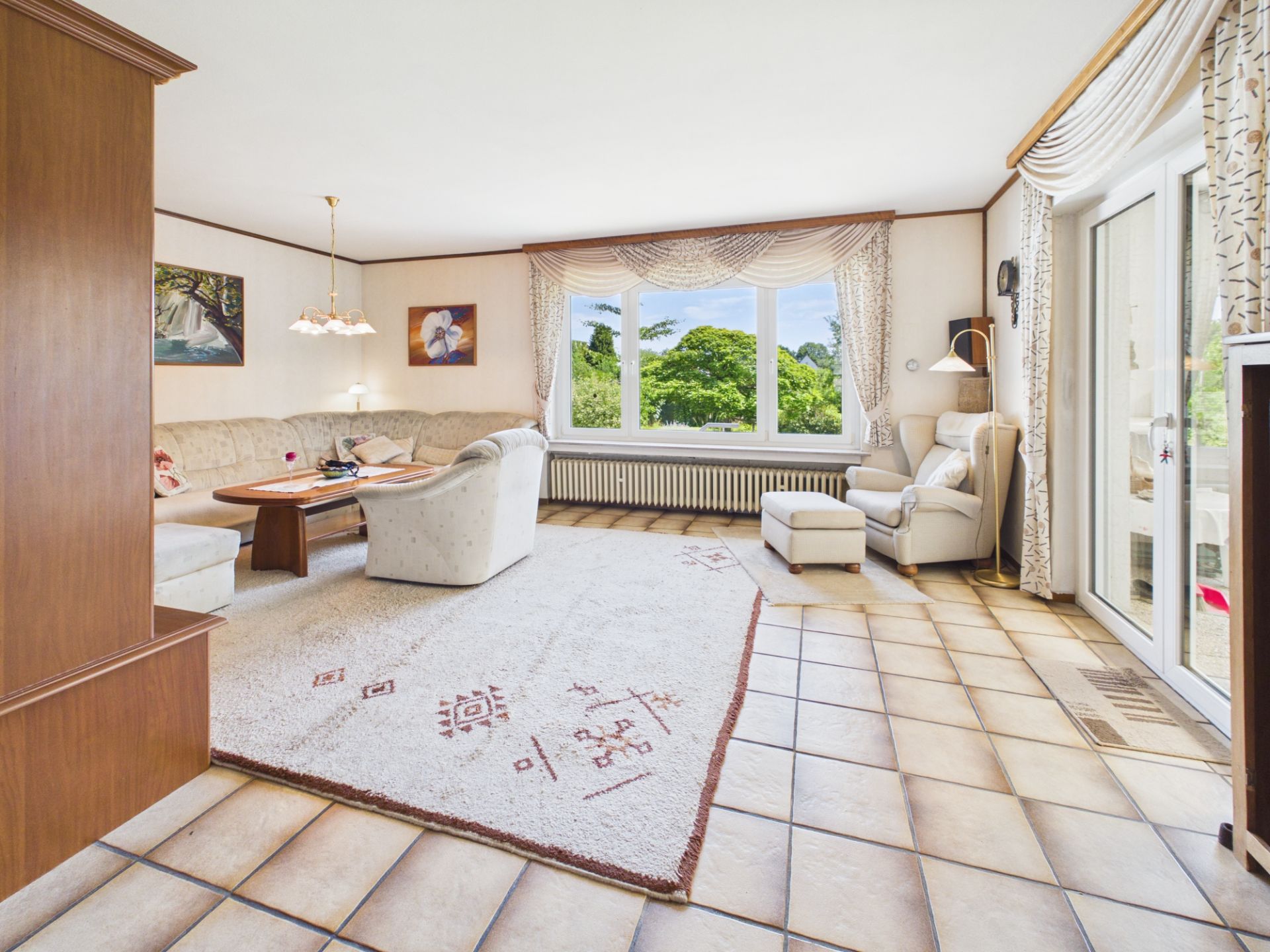 Helles Wohnzimmer mit großen Fenstern, Ecksofa, Sessel, Teppich und Esstisch.