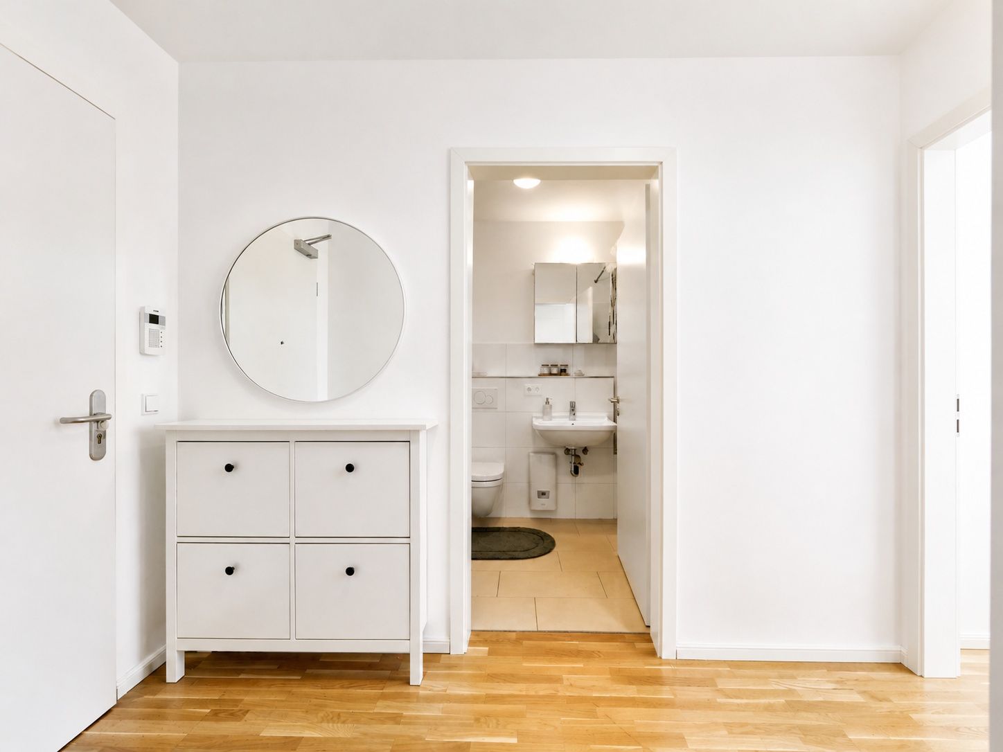 Heller Flur mit Kommode, rundem Spiegel und Blick ins Badezimmer.