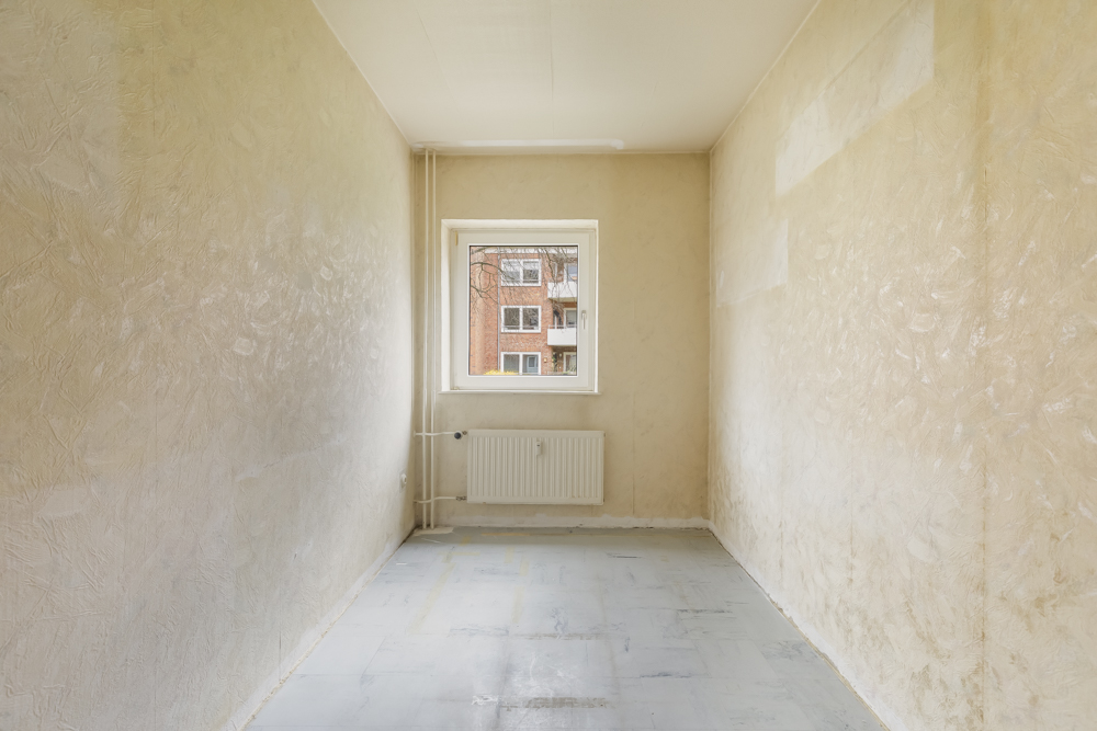 Leerer, schmaler Raum mit einem Fenster und Heizkörper an der Stirnwand.
