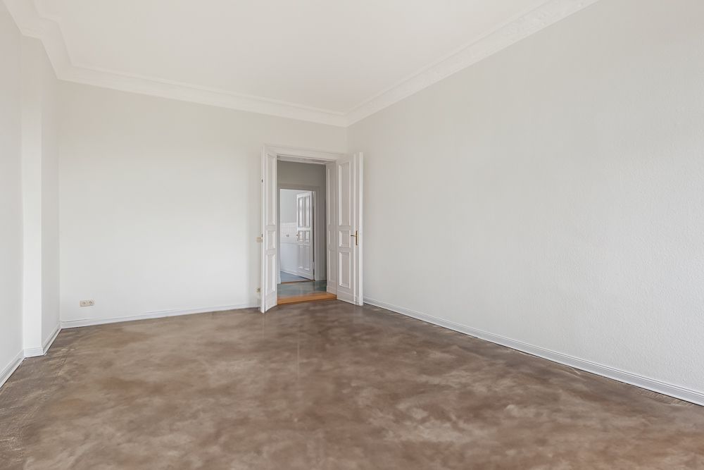 Leerer Raum mit weiß gestrichenen Wänden, braunem Boden und offener Doppeltür.