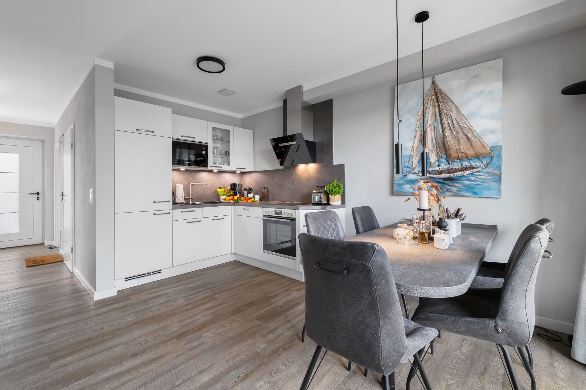 Moderne Küche mit Esstisch, vier Stühlen und einem Bild eines Segelboots an der Wand.
