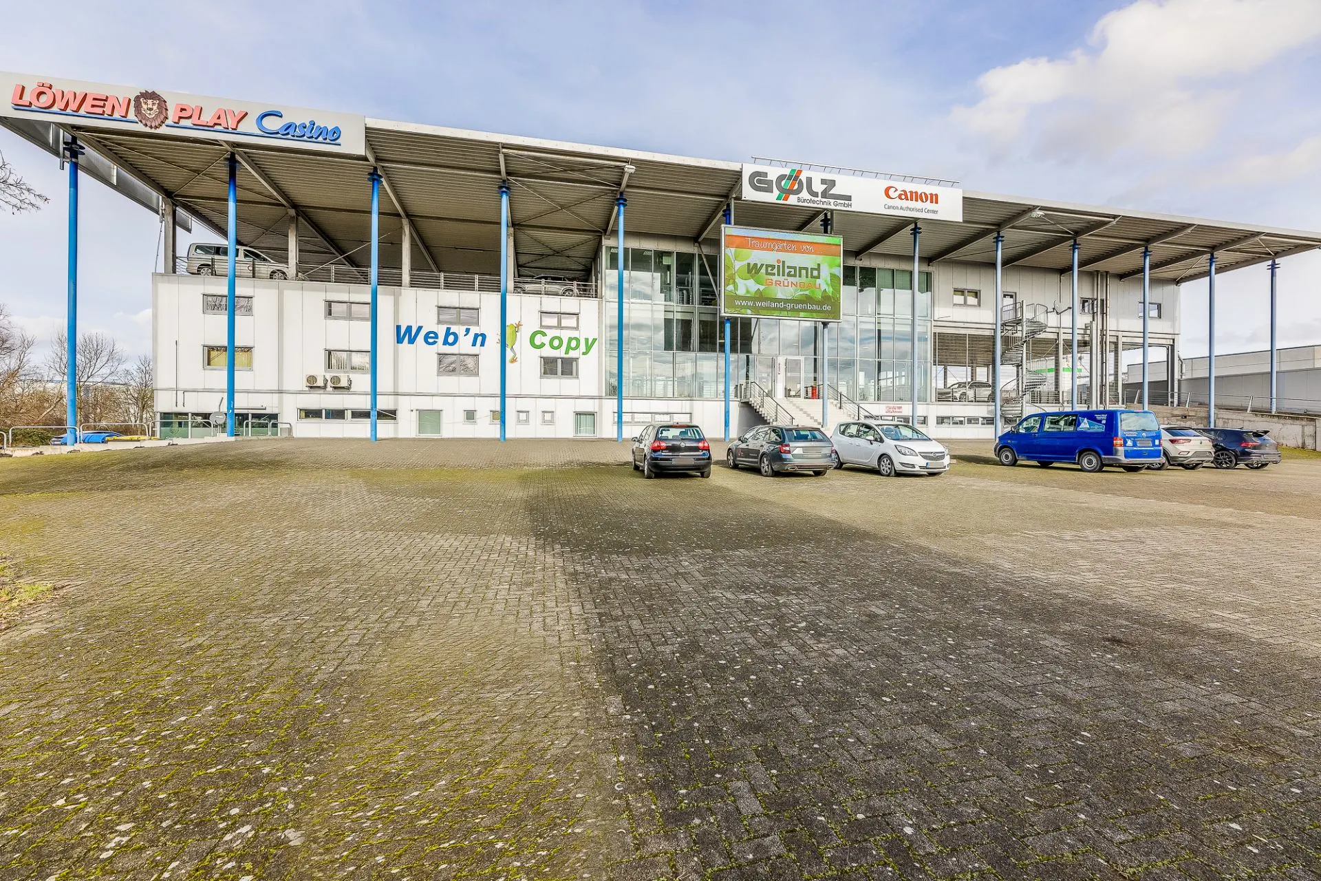Großes Geschäftsgebäude mit Glasfassade und mehreren geparkten Autos davor.