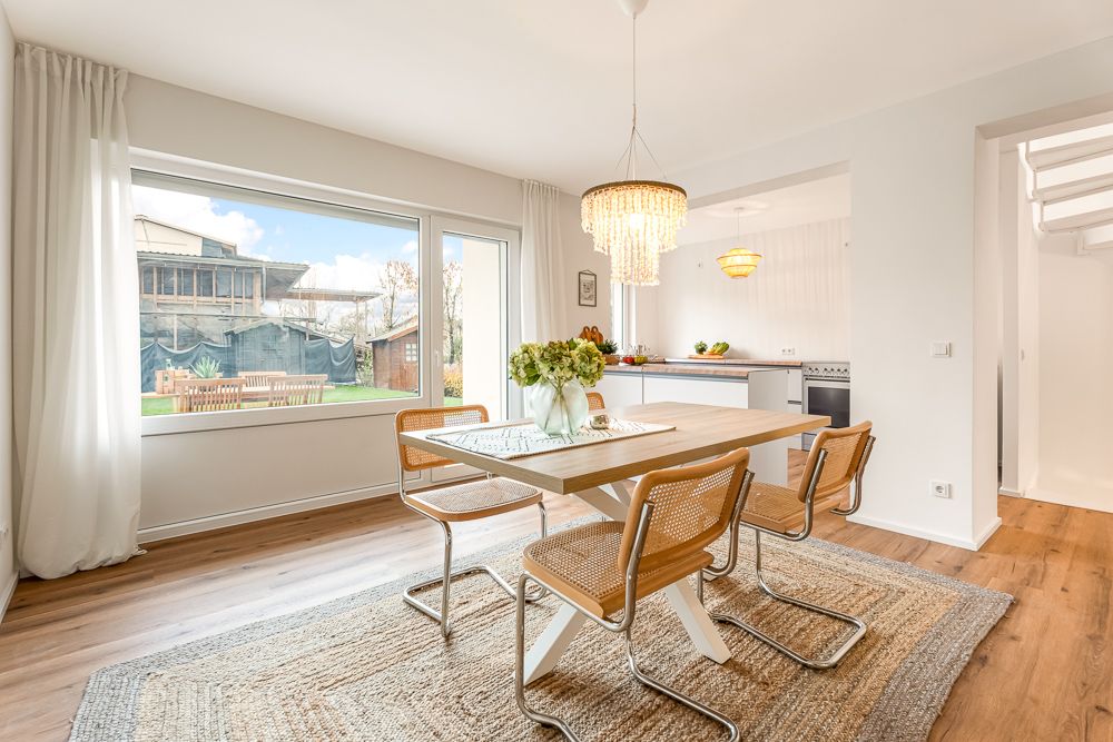 Helles Esszimmer mit Holztisch, vier Stühlen, großem Fenster und Zugang zur offenen Küche.
