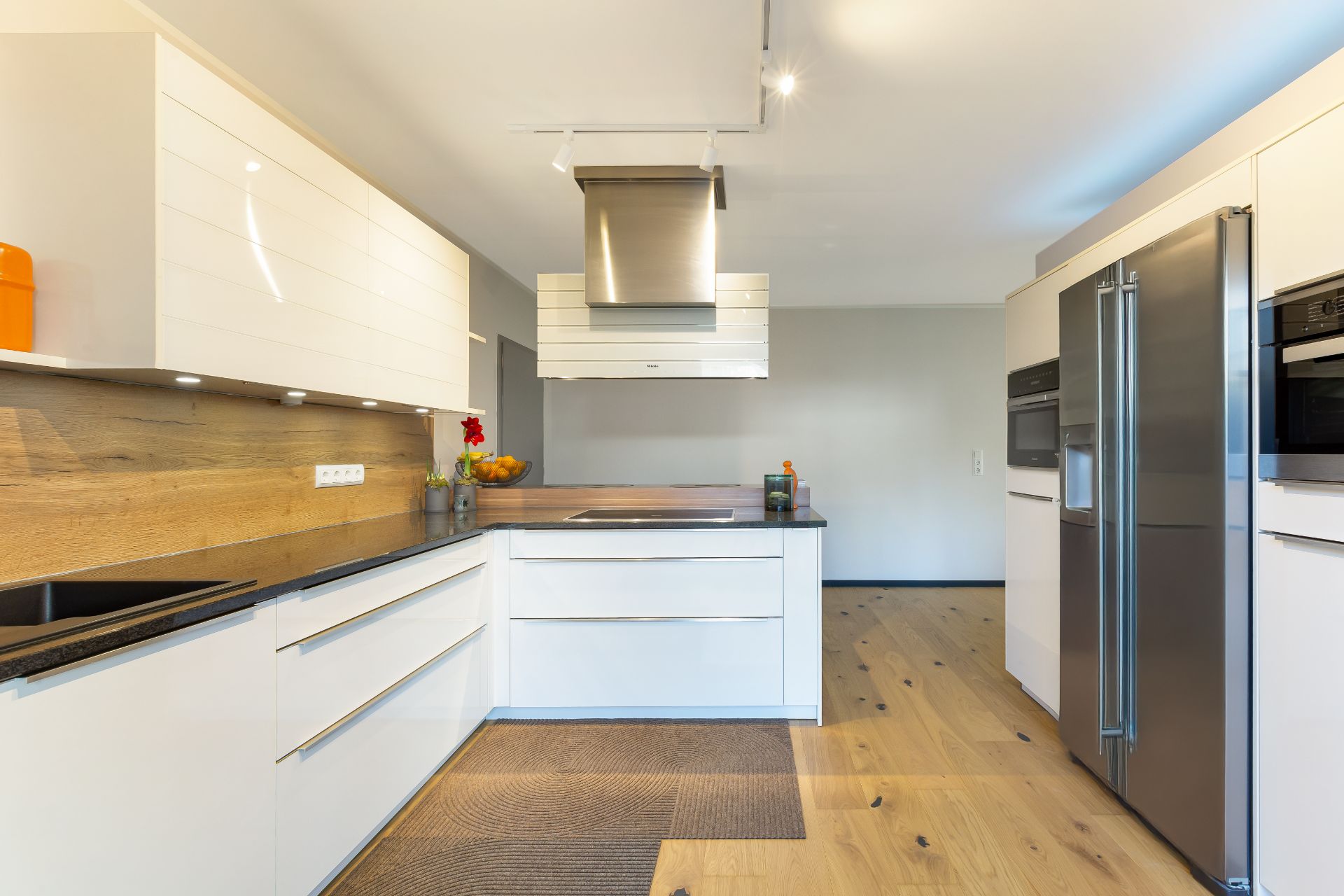 Moderne Küche mit weißen Schränken, Holzfußboden und Edelstahlgeräten.