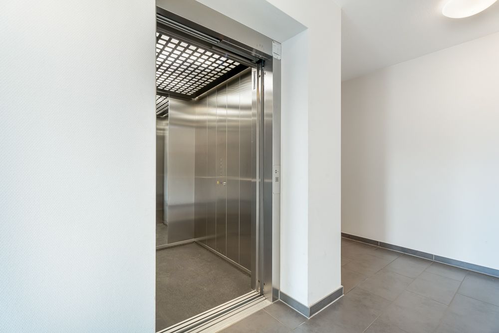 Offener Aufzug in einem hellen, modernen Flur mit Fliesenboden.