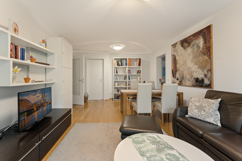 Wohnzimmer mit Sofa, Esstisch, Bücherregal, Fernseher und großem Gemälde an der Wand.