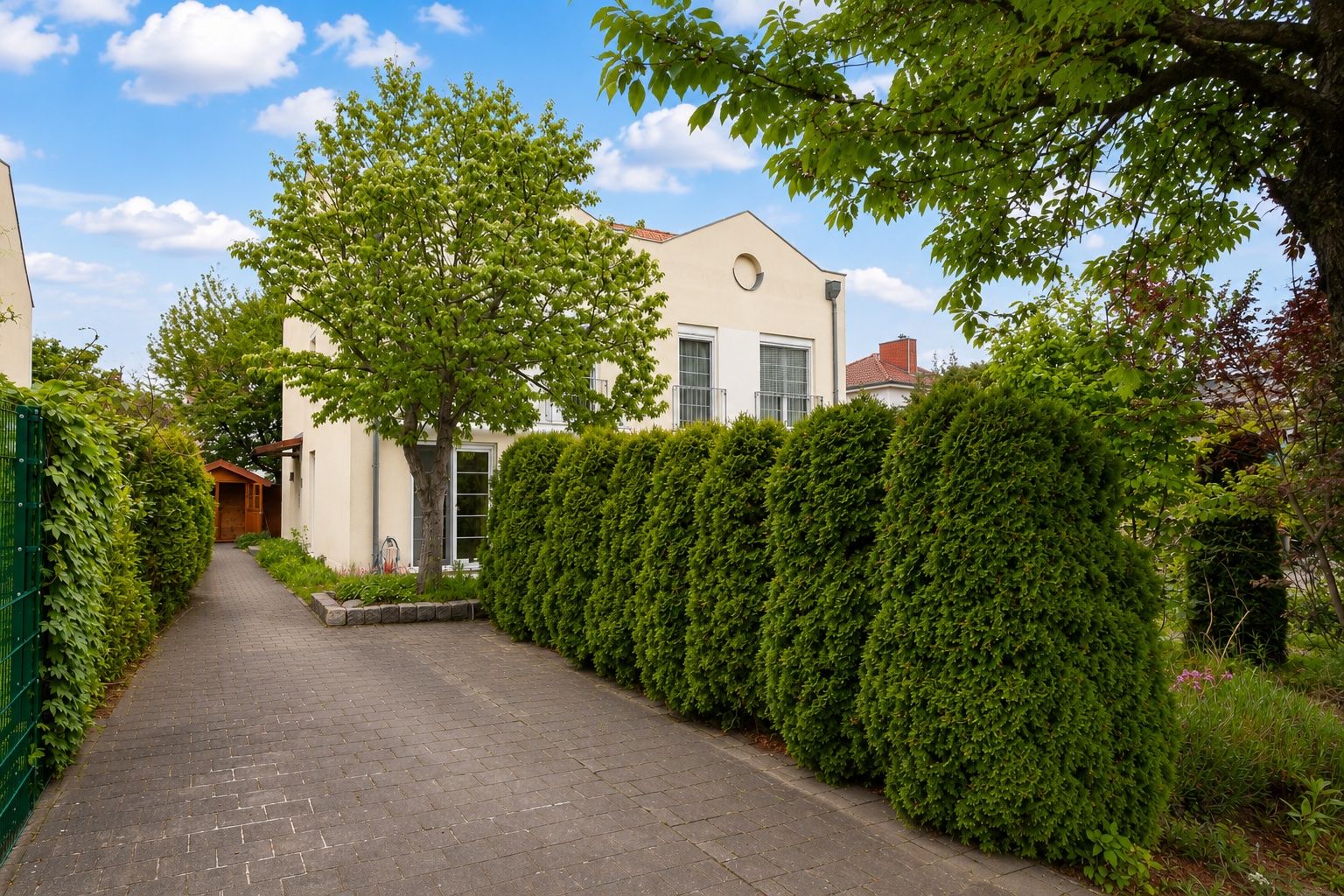 Einfamilienhaus mit heller Fassade, Auffahrt, Bäumen und gepflegter Hecke im Vorgarten.