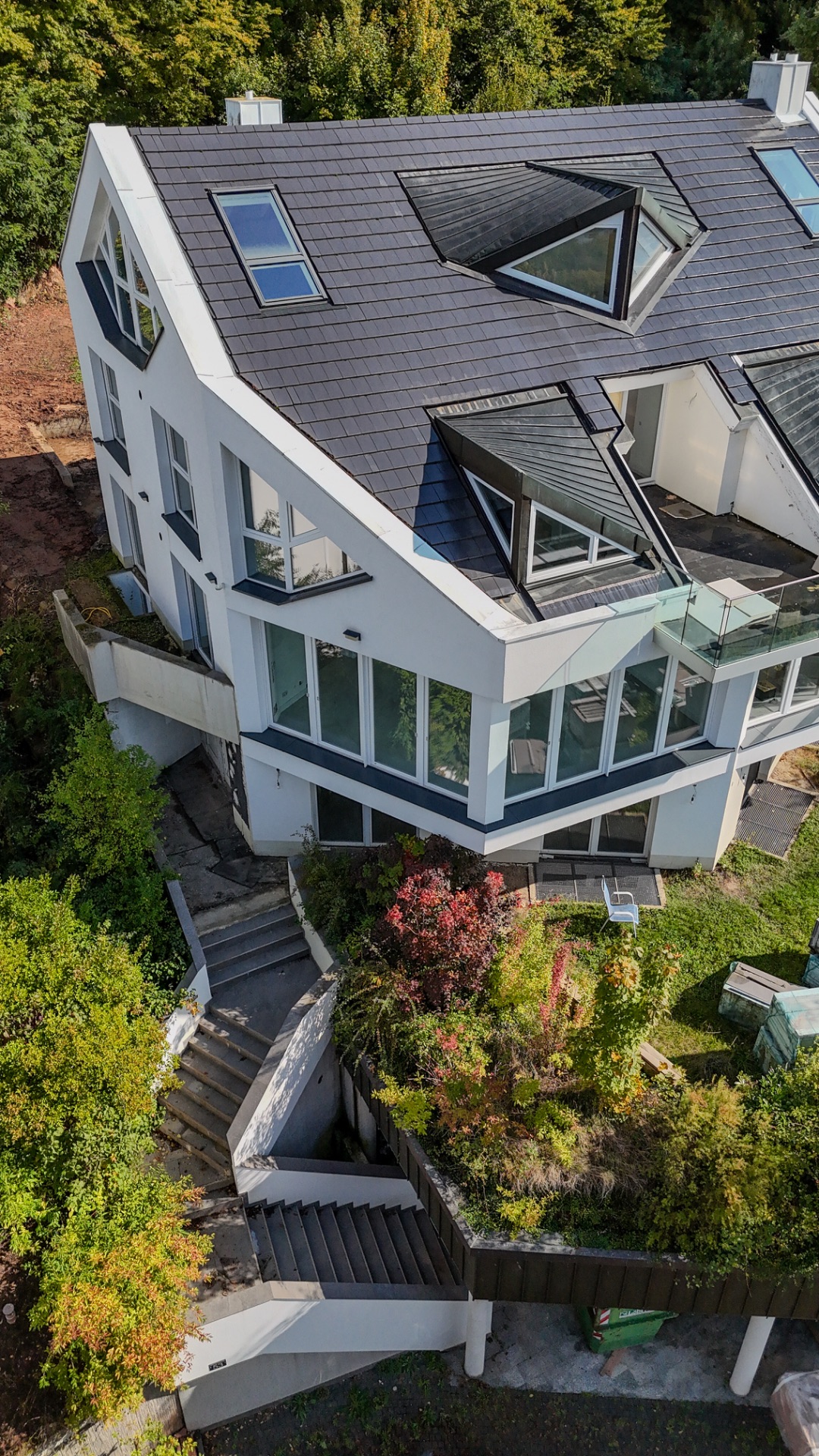 Modernes Wohnhaus mit vielen Fenstern und schrägem Dach, Außentreppe und Garten im Vordergrund.