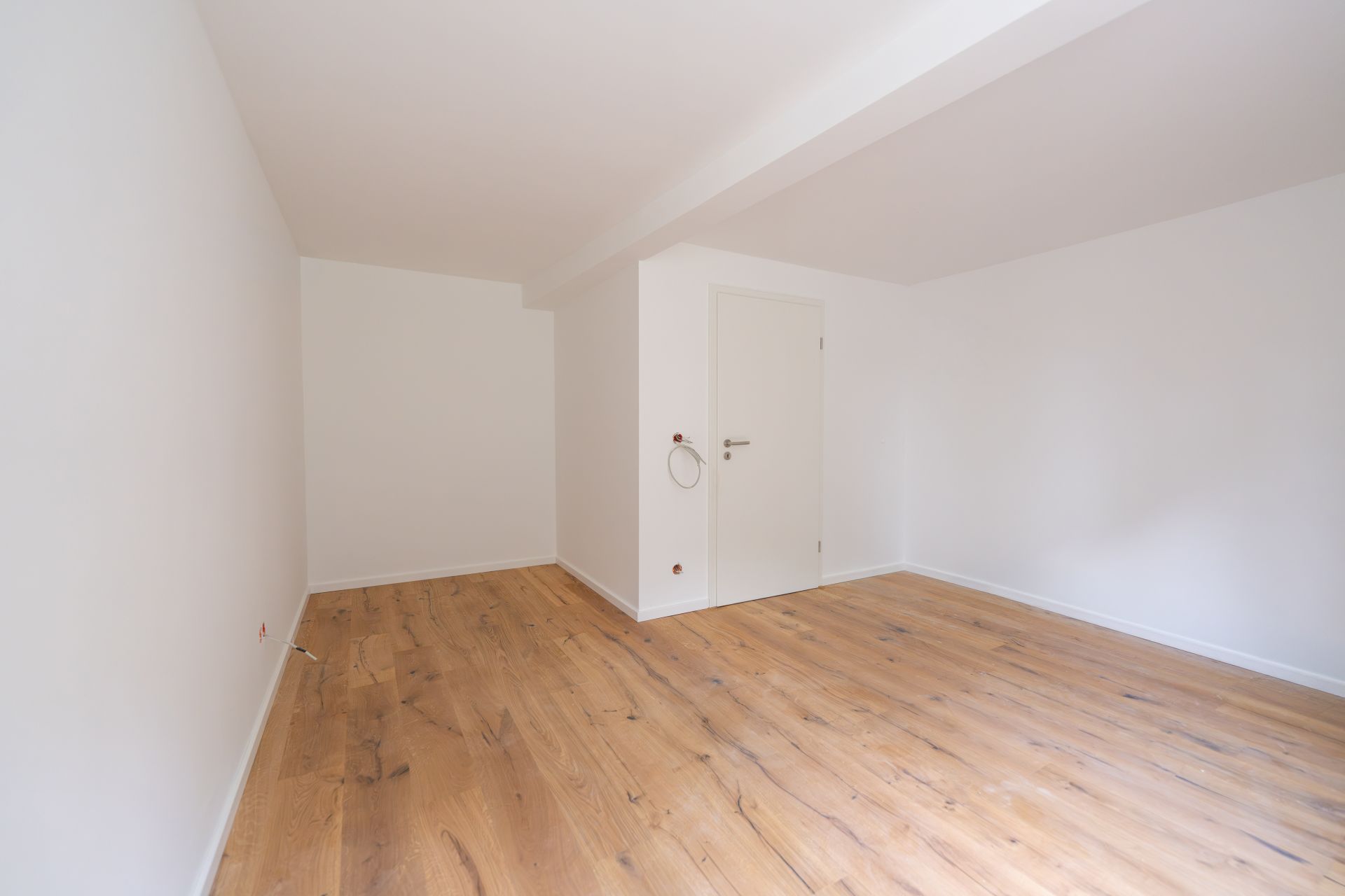Leerer Raum mit weißen Wänden, Holzboden und einer weißen Tür.