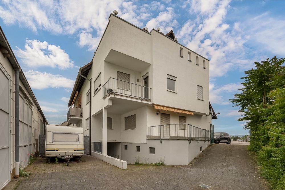 Modernes, weißes Wohnhaus mit Balkonen und einem Wohnwagen links daneben.