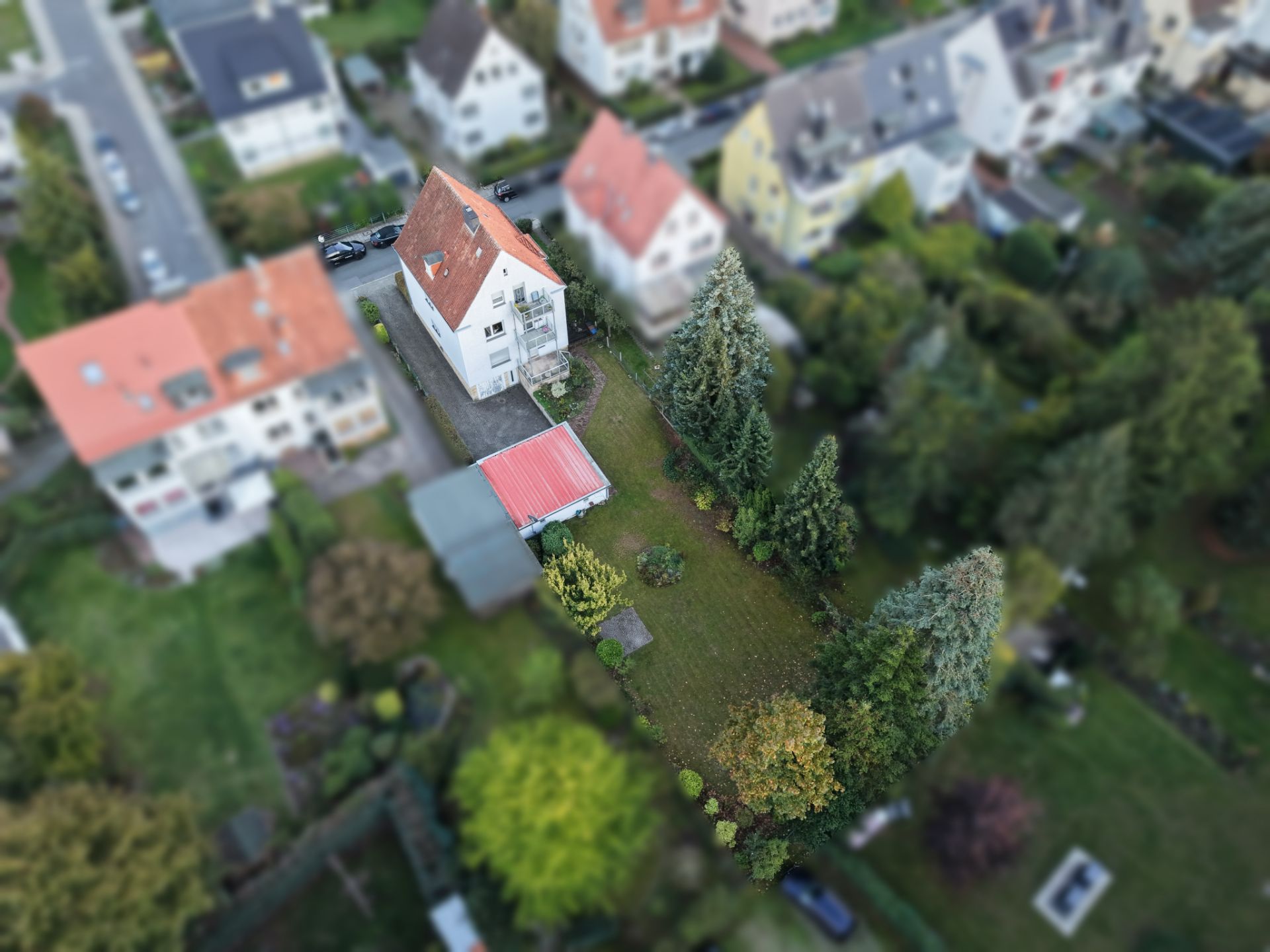 Luftaufnahme eines Einfamilienhauses mit großem Garten und Bäumen in einem Wohngebiet.