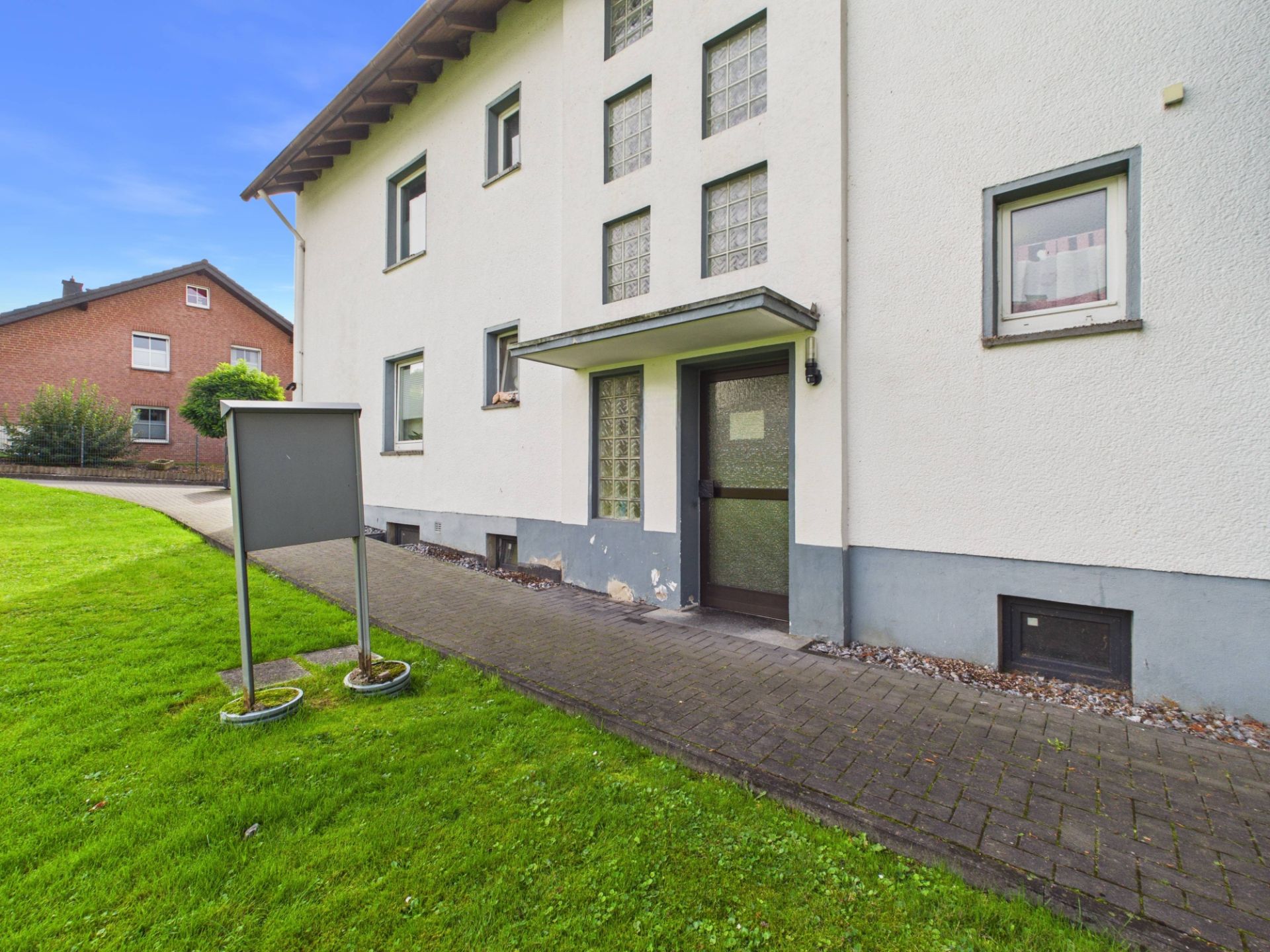 Eingang eines Wohnhauses mit Gehweg und Rasenfläche im Vordergrund.