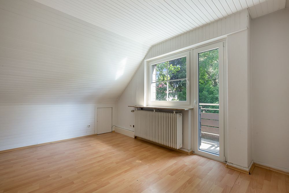 Heller Raum mit schräger Decke, großem Fenster, Tür zum Balkon und Heizkörper.