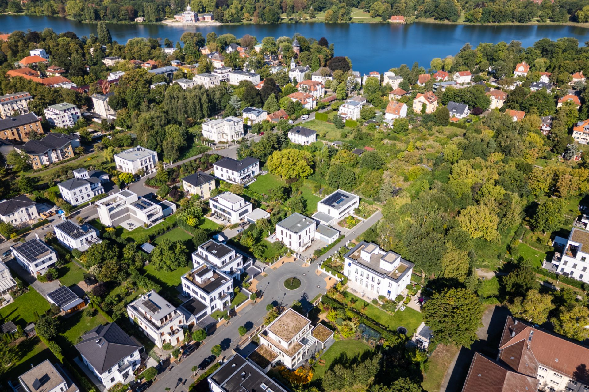 Luftaufnahme eines Wohngebiets mit Häusern, Straßen und viel Grün, im Hintergrund ein See.