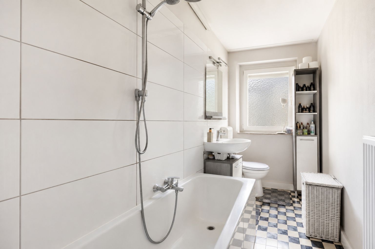 Helles Badezimmer mit Badewanne, Waschbecken, Toilette, Regal und Fenster.