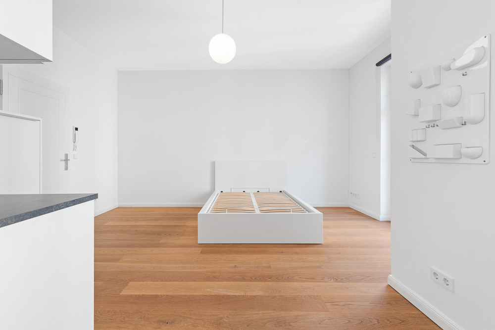 Helles Schlafzimmer mit Holzfußboden und weißem Bettgestell ohne Matratze.