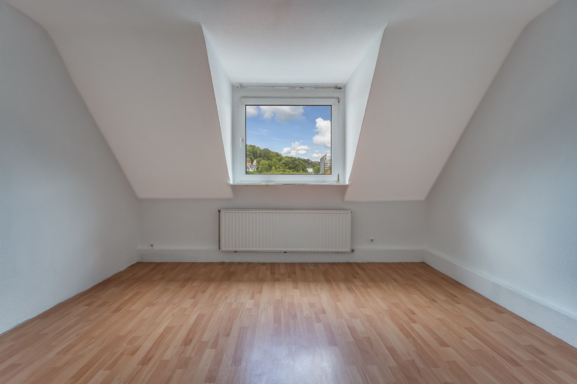 Leerer Raum mit Dachschräge, Fenster und Heizung, heller Laminatboden.