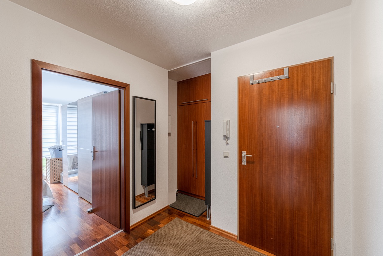 Flur mit Holztüren, Spiegel, Schrank und Blick in ein helles Zimmer mit Parkettboden.