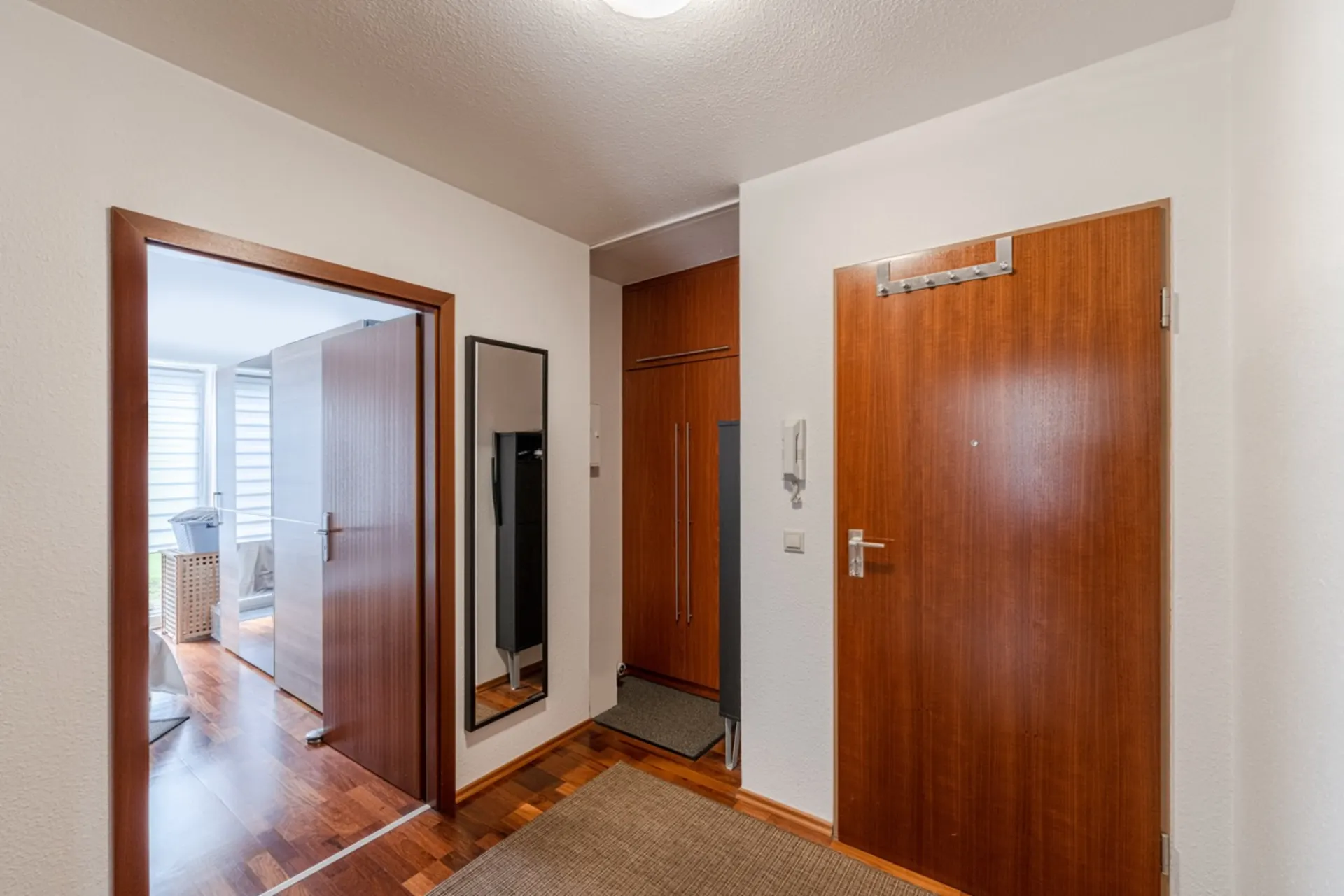 Flur mit Holztüren, Spiegel, Schrank und Blick in ein helles Zimmer mit Parkettboden.